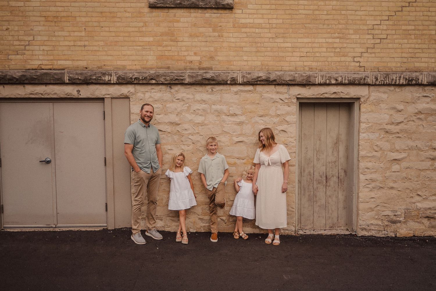 Family photo session against a rustic brick wall exterior showing casual, relaxed poses.