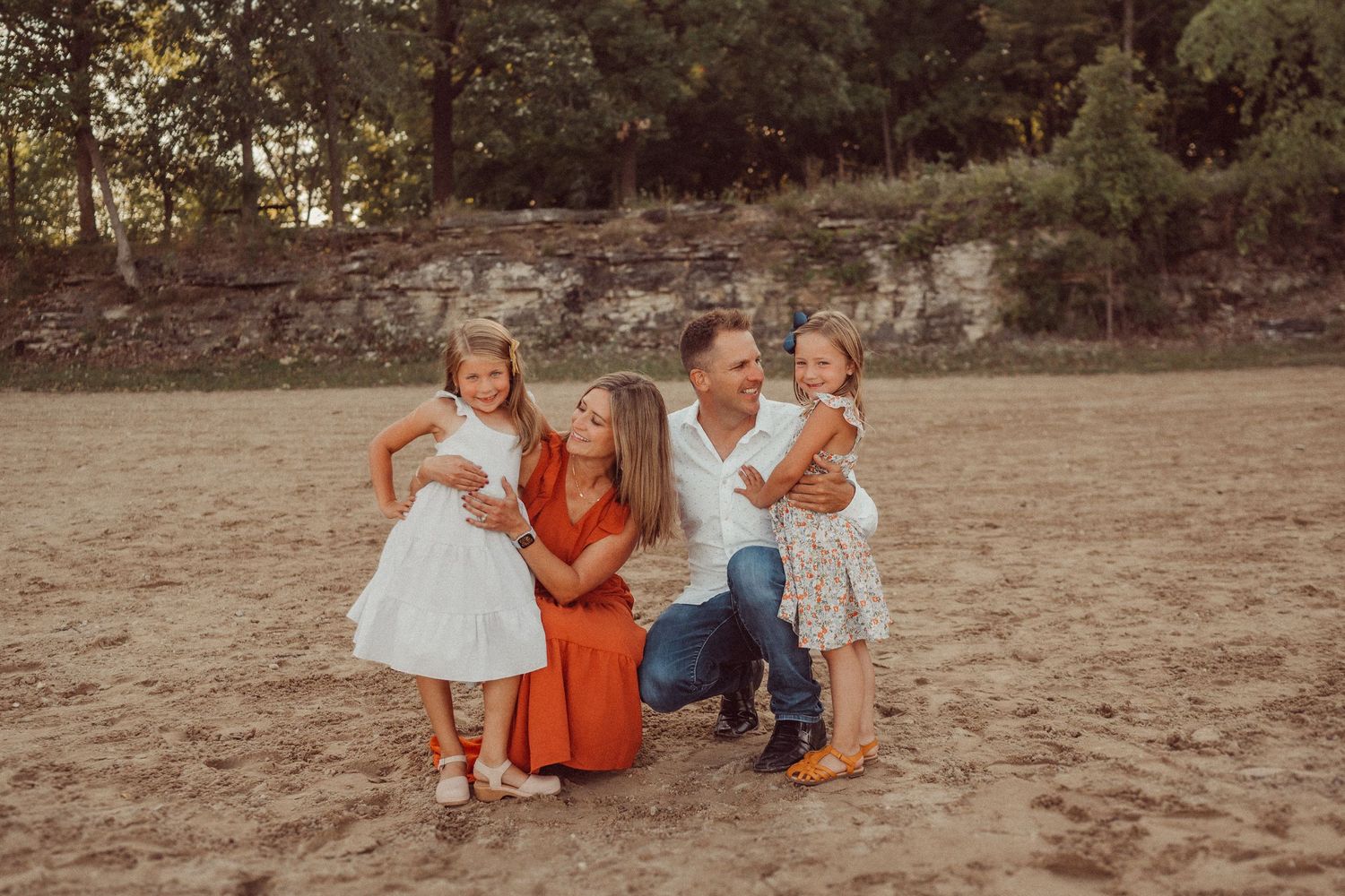 A family group portrait in casual attire against a rustic stone wall backdrop.