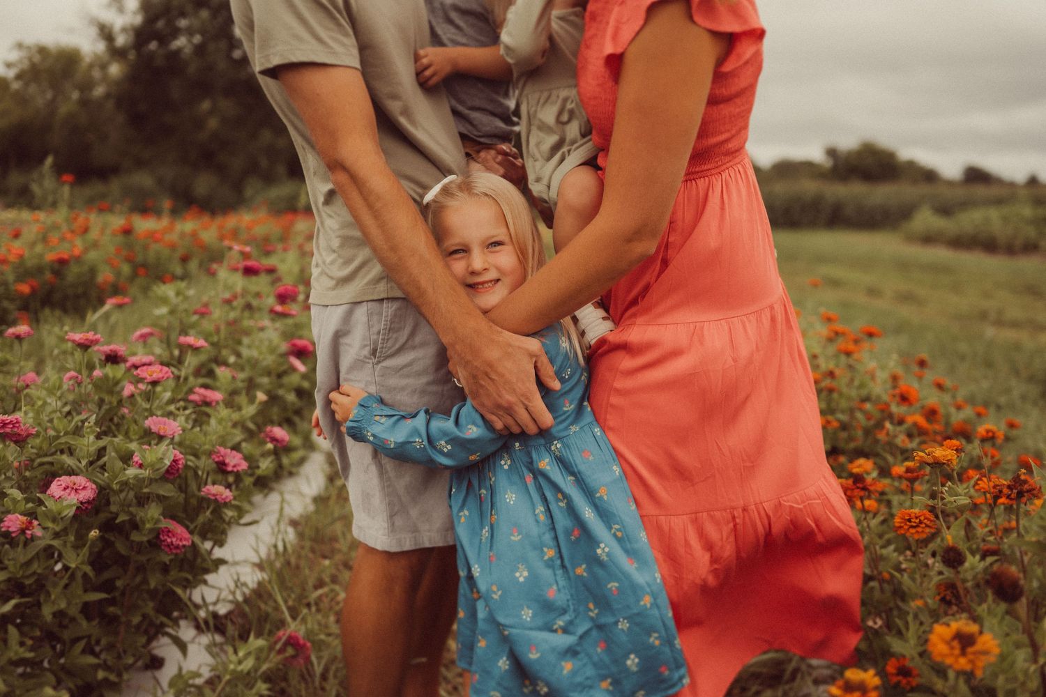 A joyful moment in a flower garden as a blue-dressed figure embraces loved ones among colorful blooms.