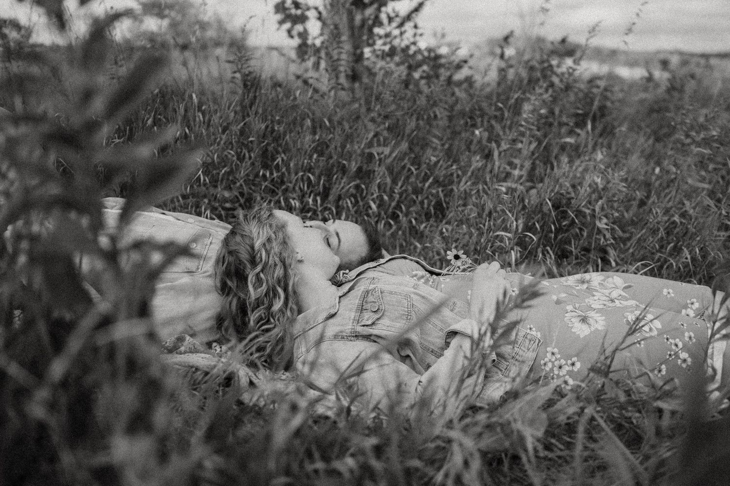 A couple rests together in tall grass captured in dreamy black and white.
