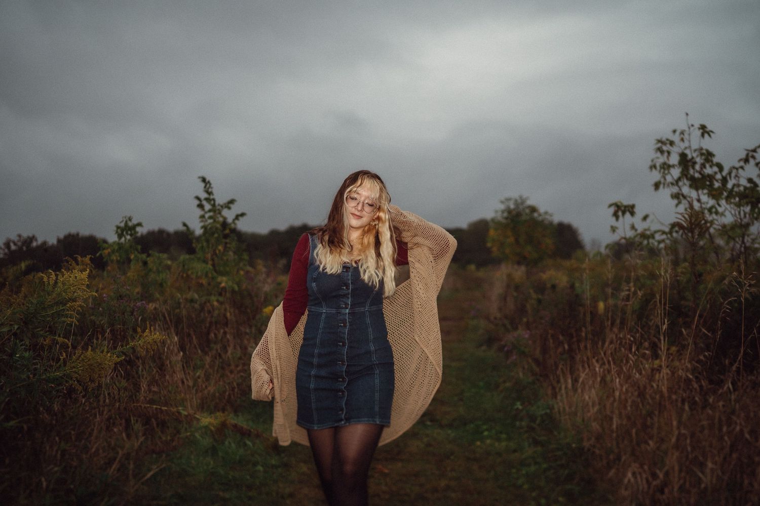 Moody outdoor portrait in denim dress and cardigan against stormy sky.
