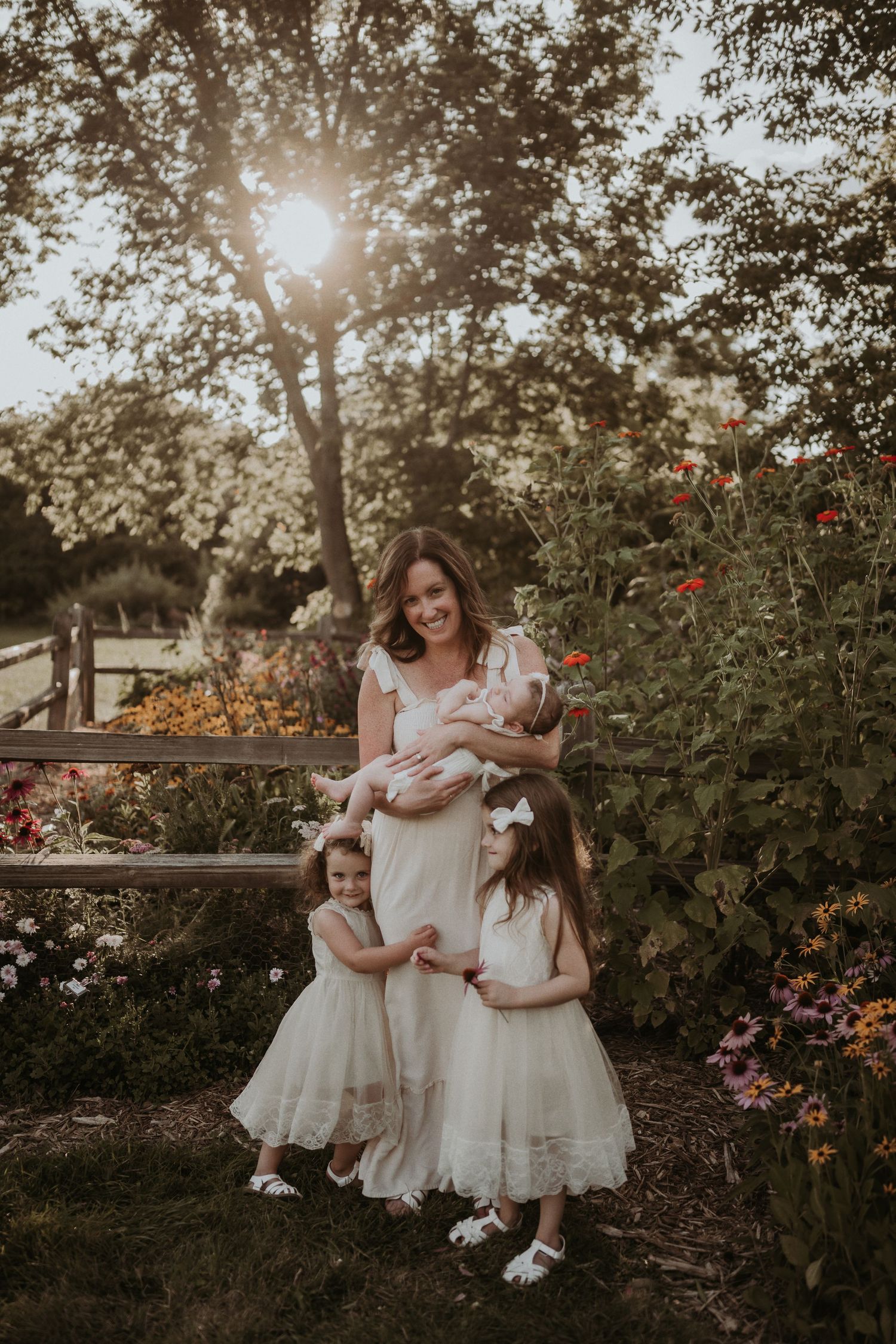 An intimate family portrait in a garden setting with matching white dresses and natural sunlight.
