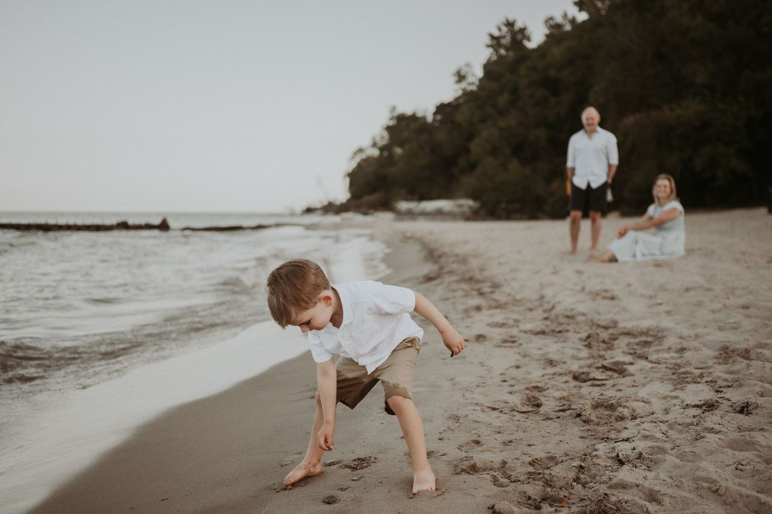 Child bending down to explore the sandy beach while others watch in the distance.