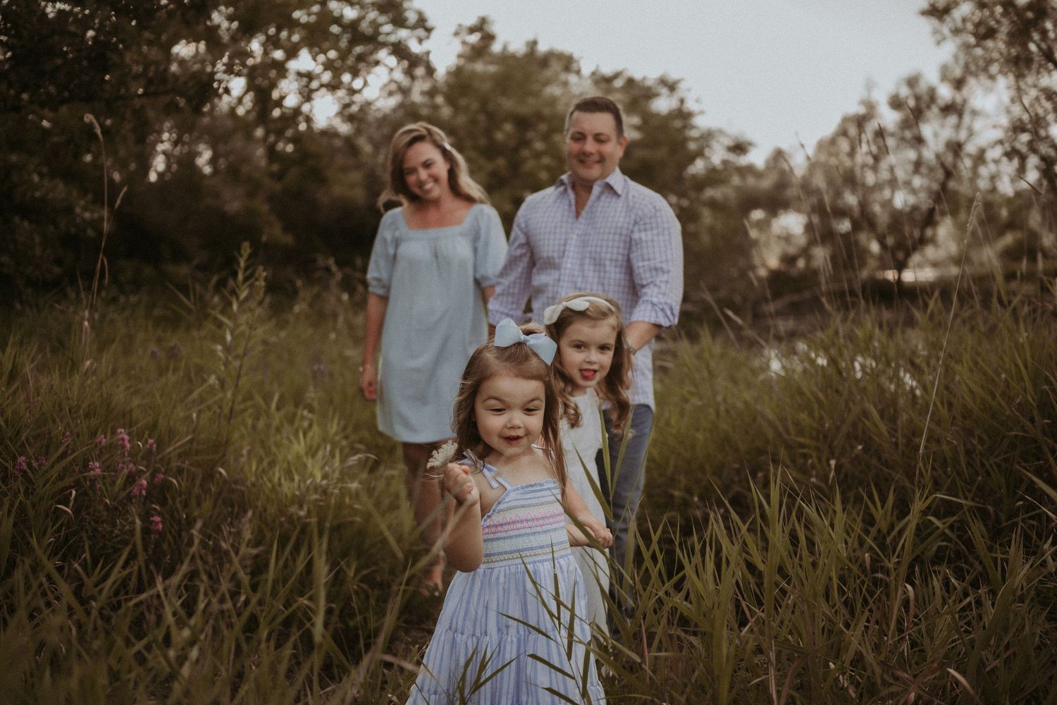 A family poses together in a field of tall grass at golden hour.