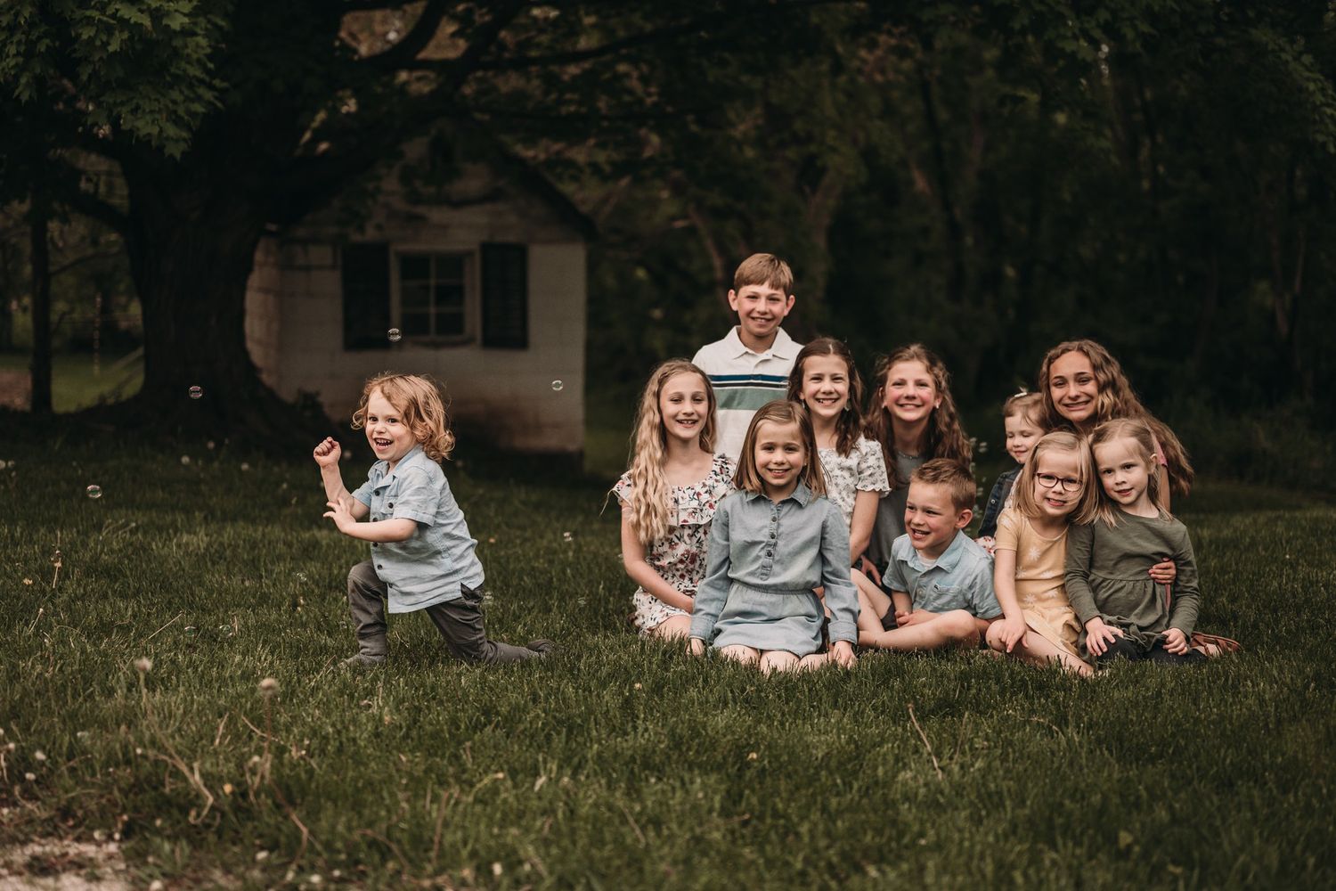 Group of children and adults sitting together on grass in front of a house.