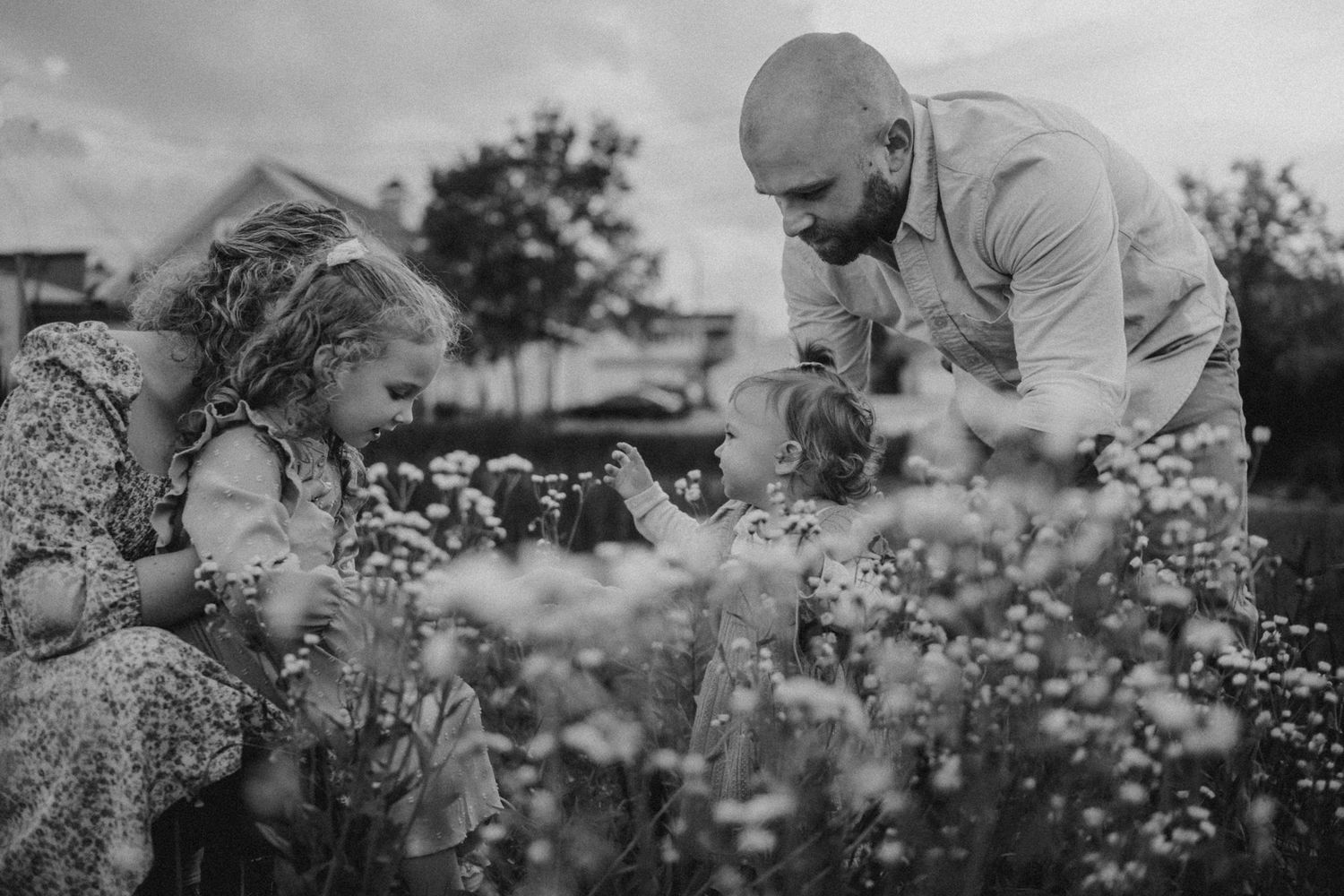 A black and white photo of a family exploring wildflowers together in a field.