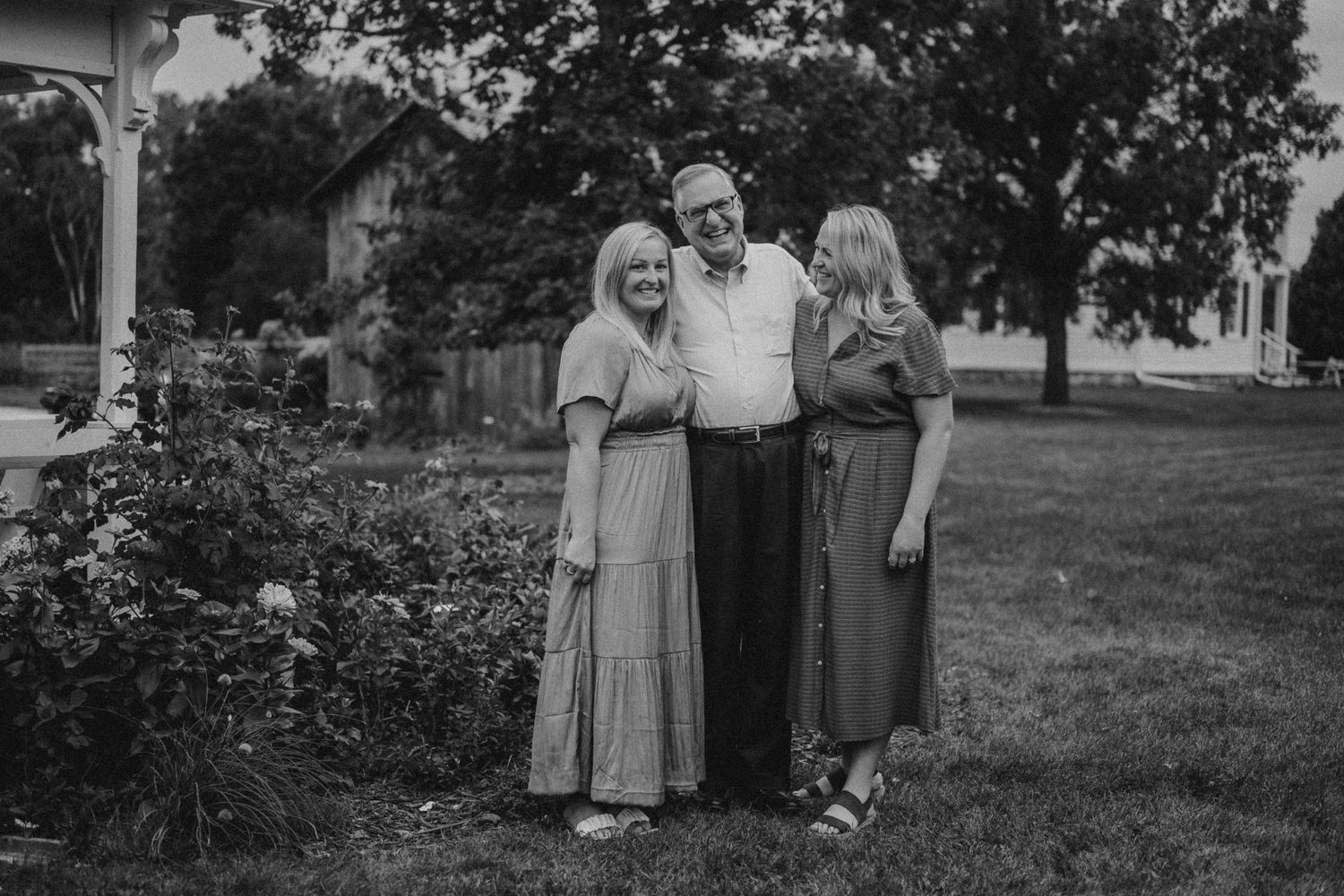 Black and white portrait of three people standing together in a garden setting.