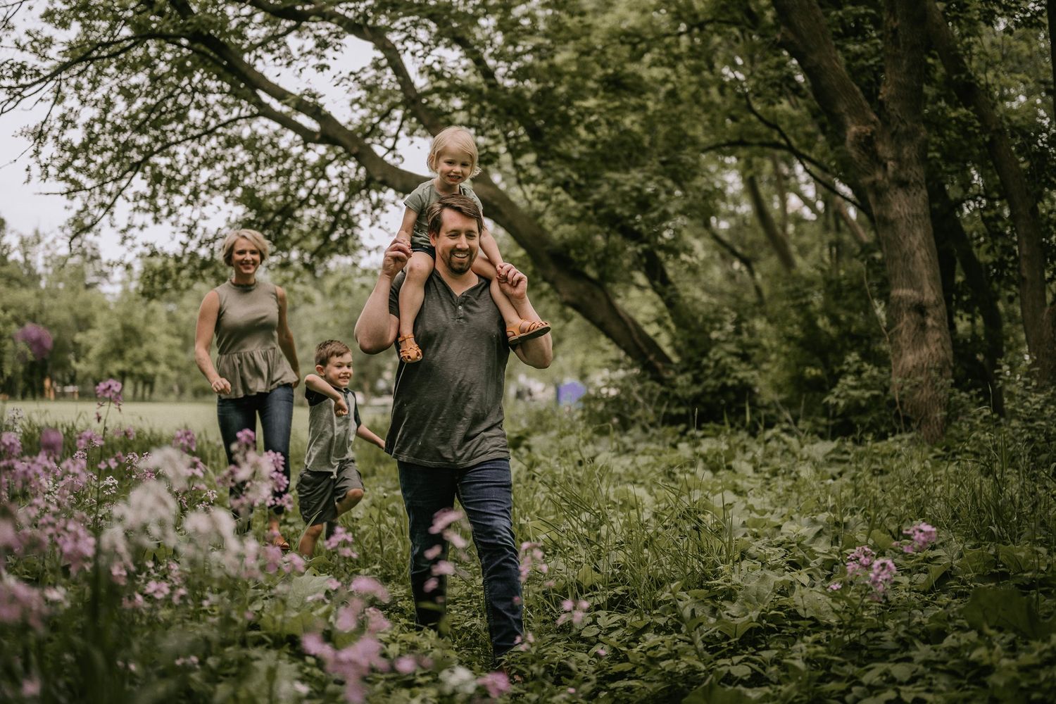 Family walks together through a wooded trail with flowering plants and trees.