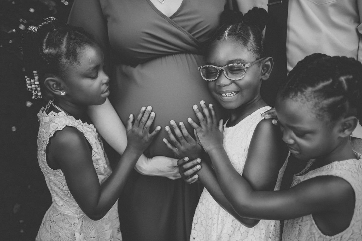 Black and white image of children gathering around and touching a pregnant belly.