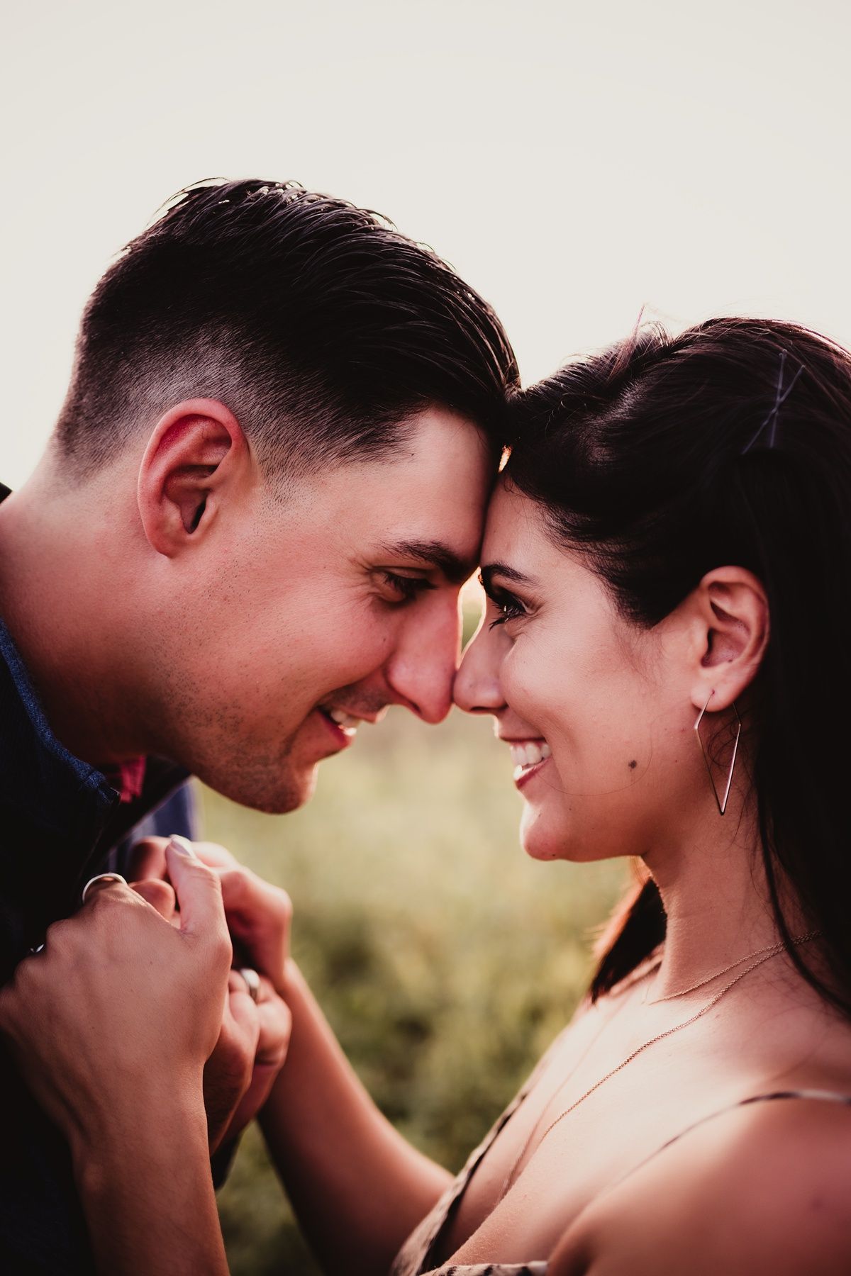 Couple shares intimate forehead touch while holding hands during sunset photoshoot.