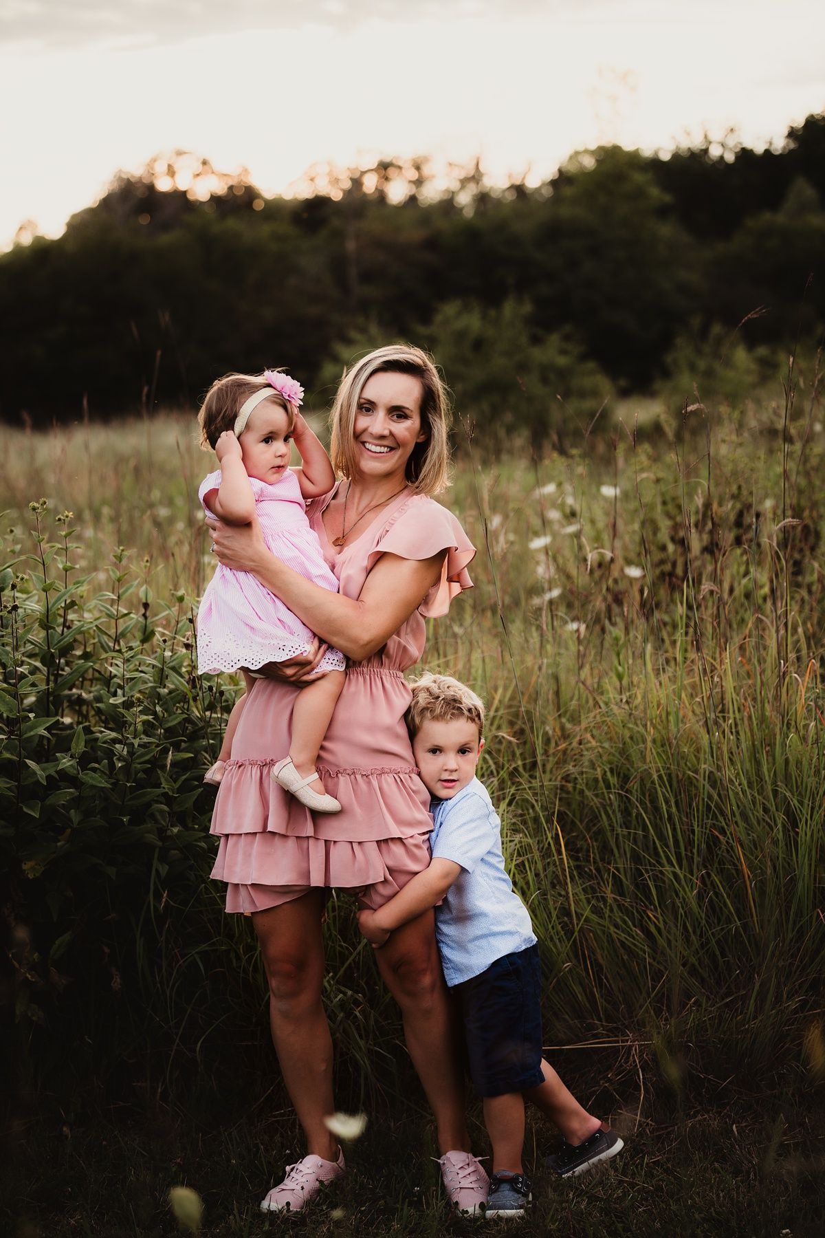 Family portrait at sunset with coordinated pink and blue outfits in tall grass.