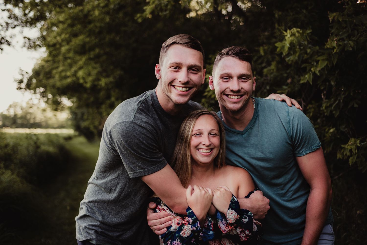 Three people share a close embrace while smiling outdoors.