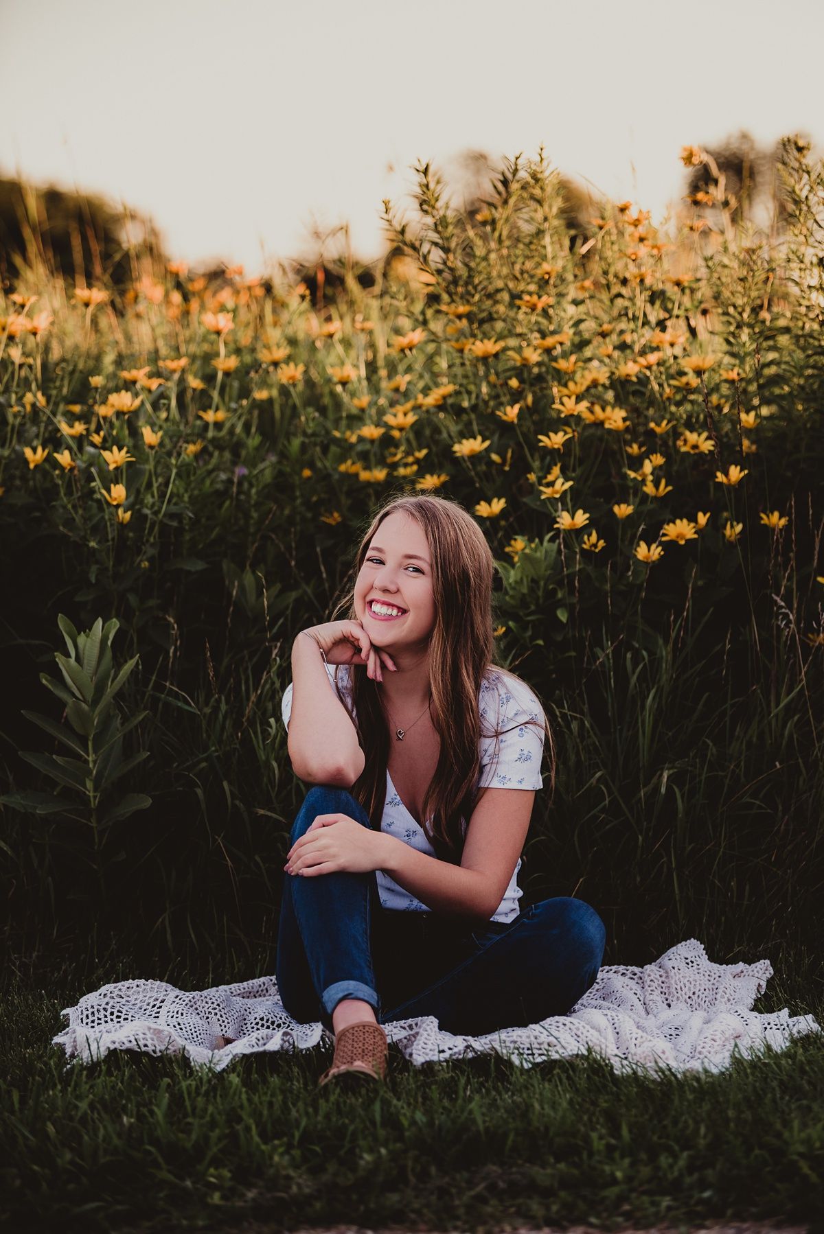 A relaxed portrait sitting on a blanket among yellow wildflowers at dusk.