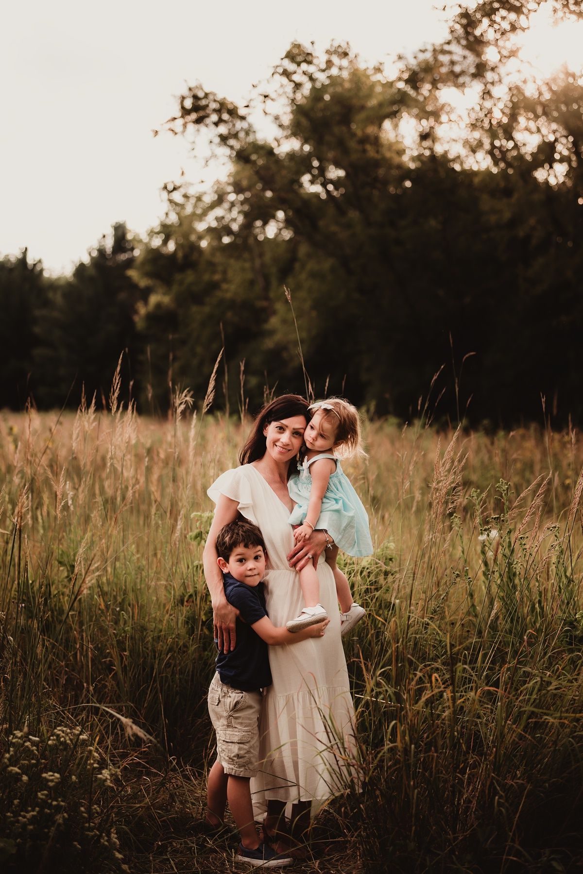 Family portrait in tall grass field during golden hour.