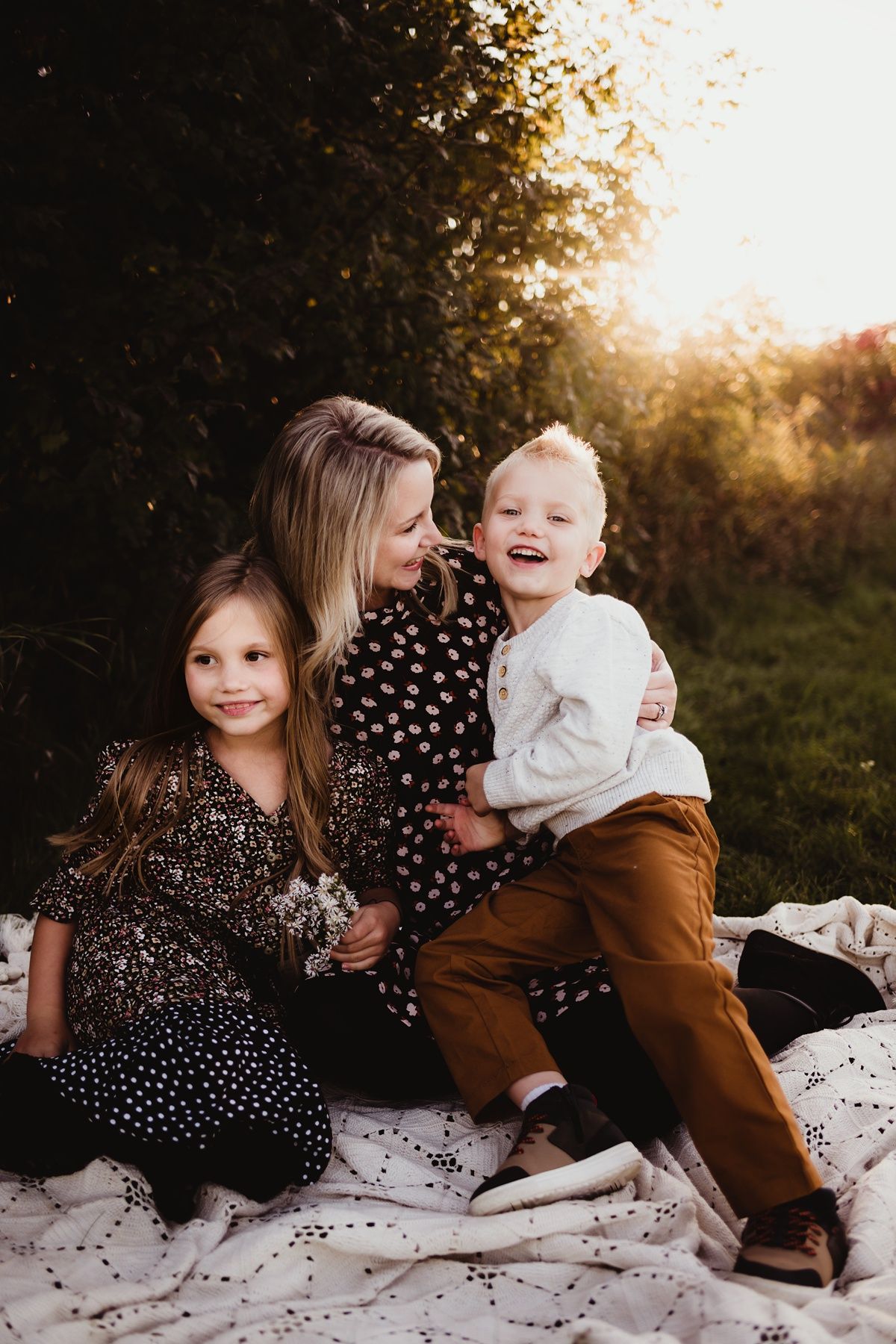 Family sitting together on white blanket during sunset photoshoot in nature.