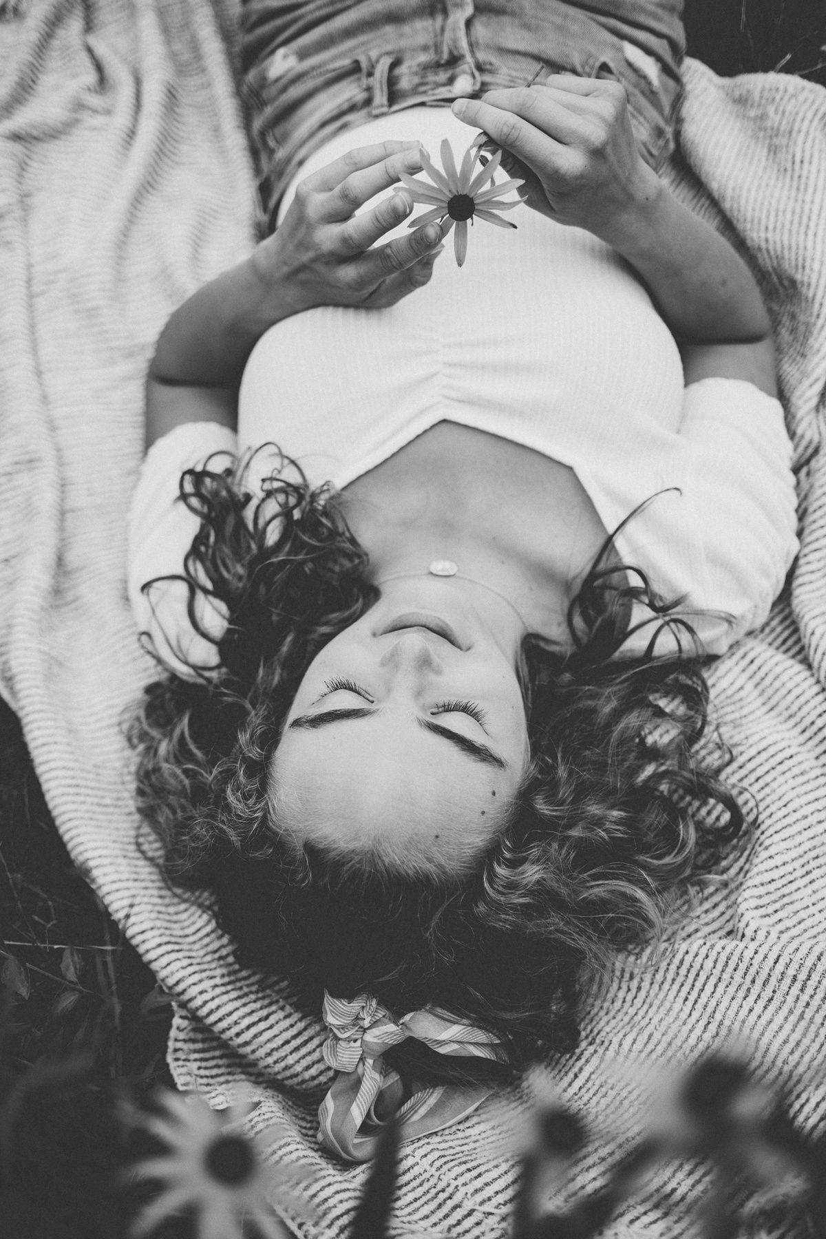 Black and white overhead shot of someone lying on blanket holding flowers.