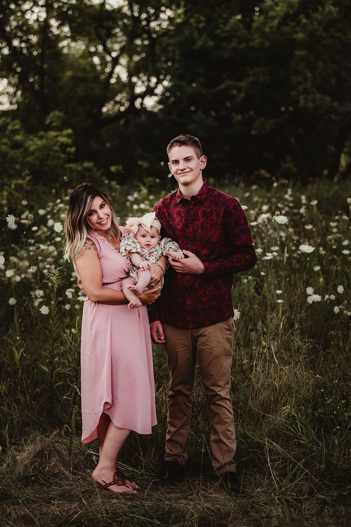 A family poses together in a wildflower field at sunset with coordinated pink and burgundy outfits.
