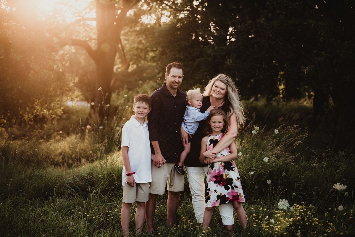 A family of five shares a candid laughing moment during golden hour in a field.