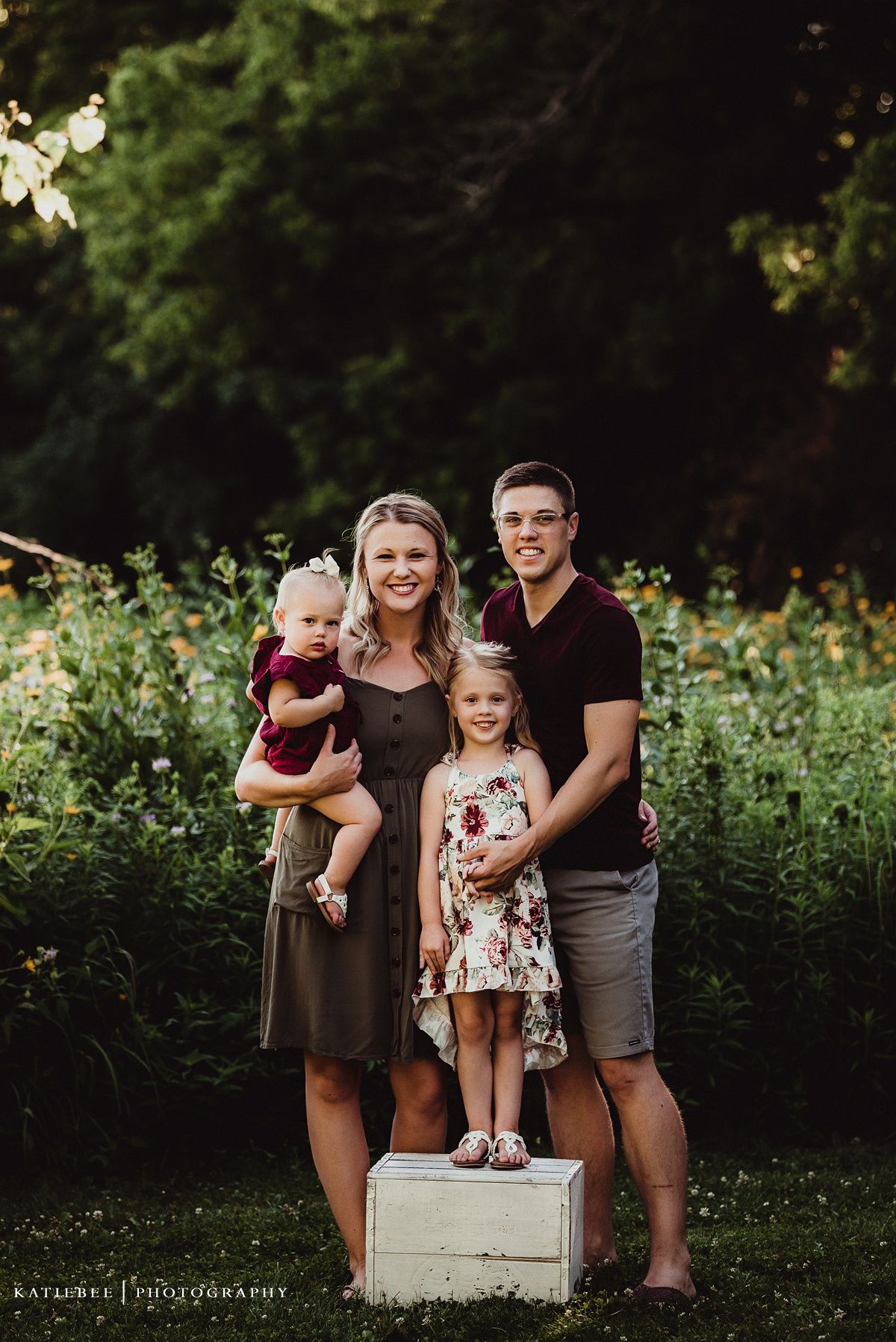 Small family poses together in garden with child standing on white box.