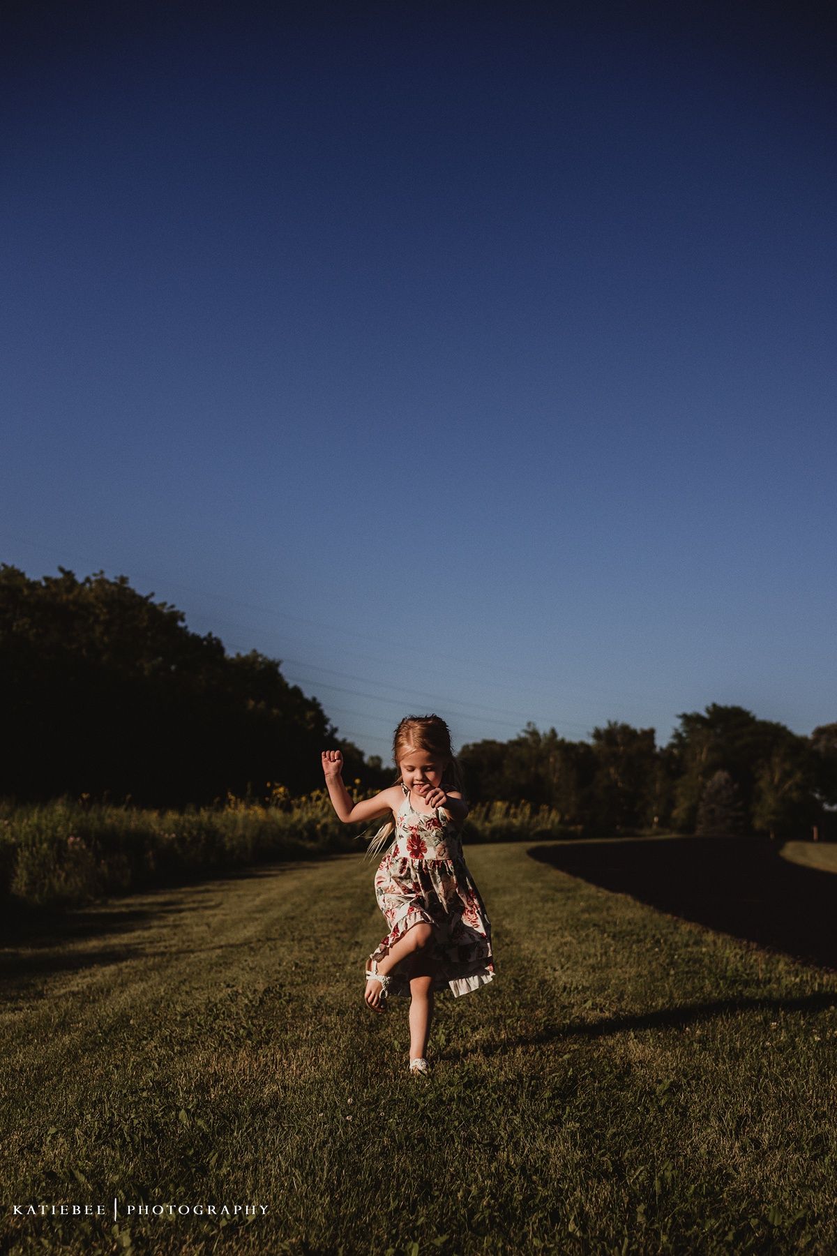 Young child in floral dress running and playing in grassy field at sunset.