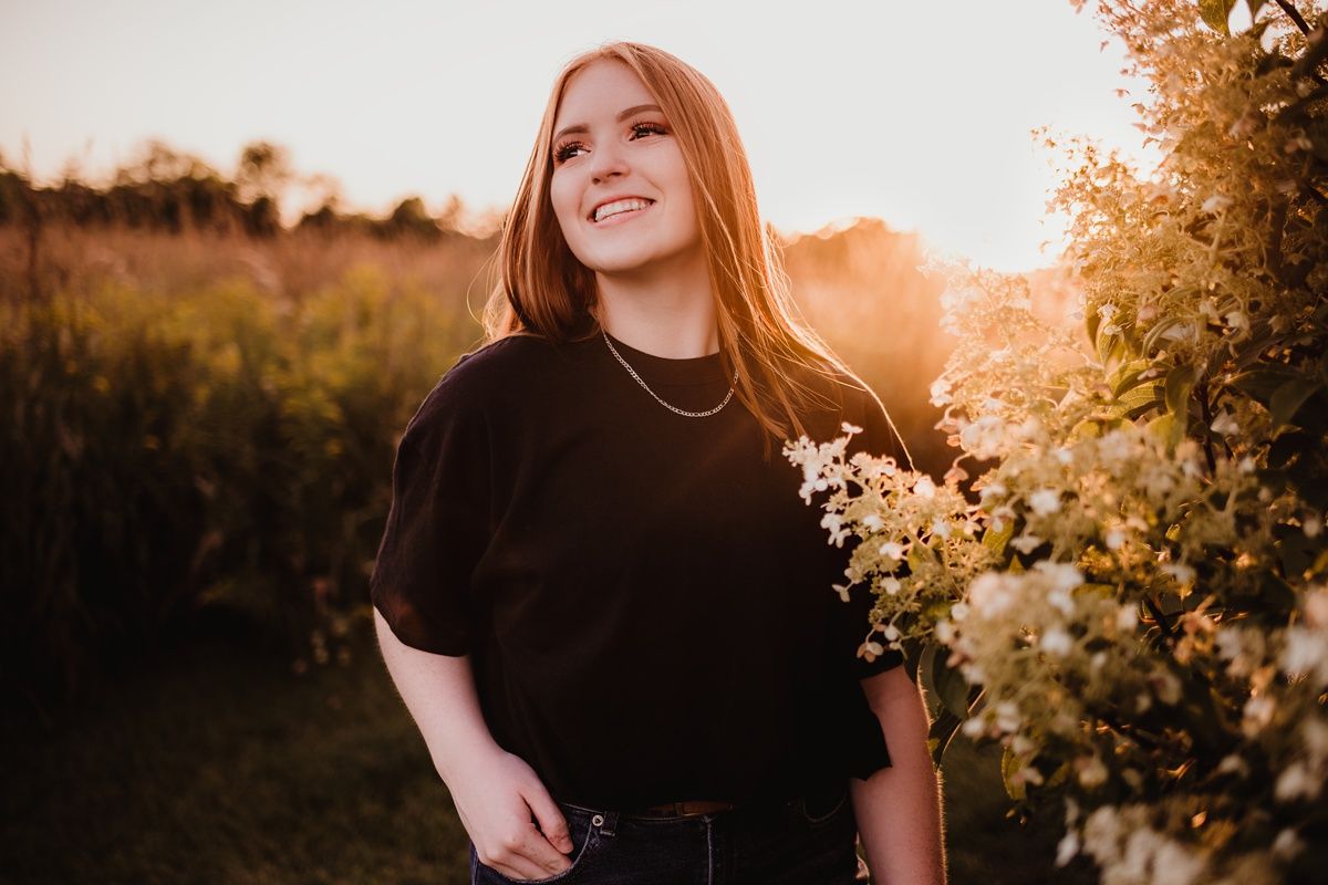 Person in black holding wildflowers during sunset in nature.