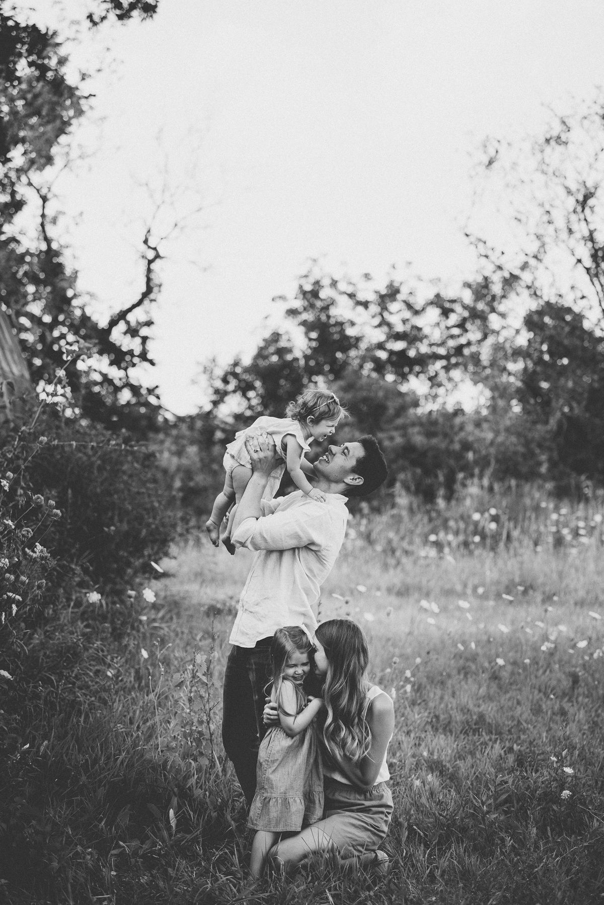 Black and white photograph of a family sharing a playful moment in a meadow.