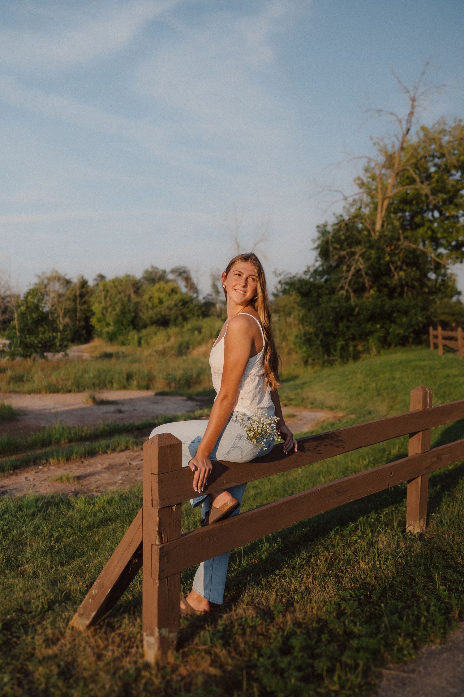 Person sitting casually on wooden fence during golden hour photoshoot.