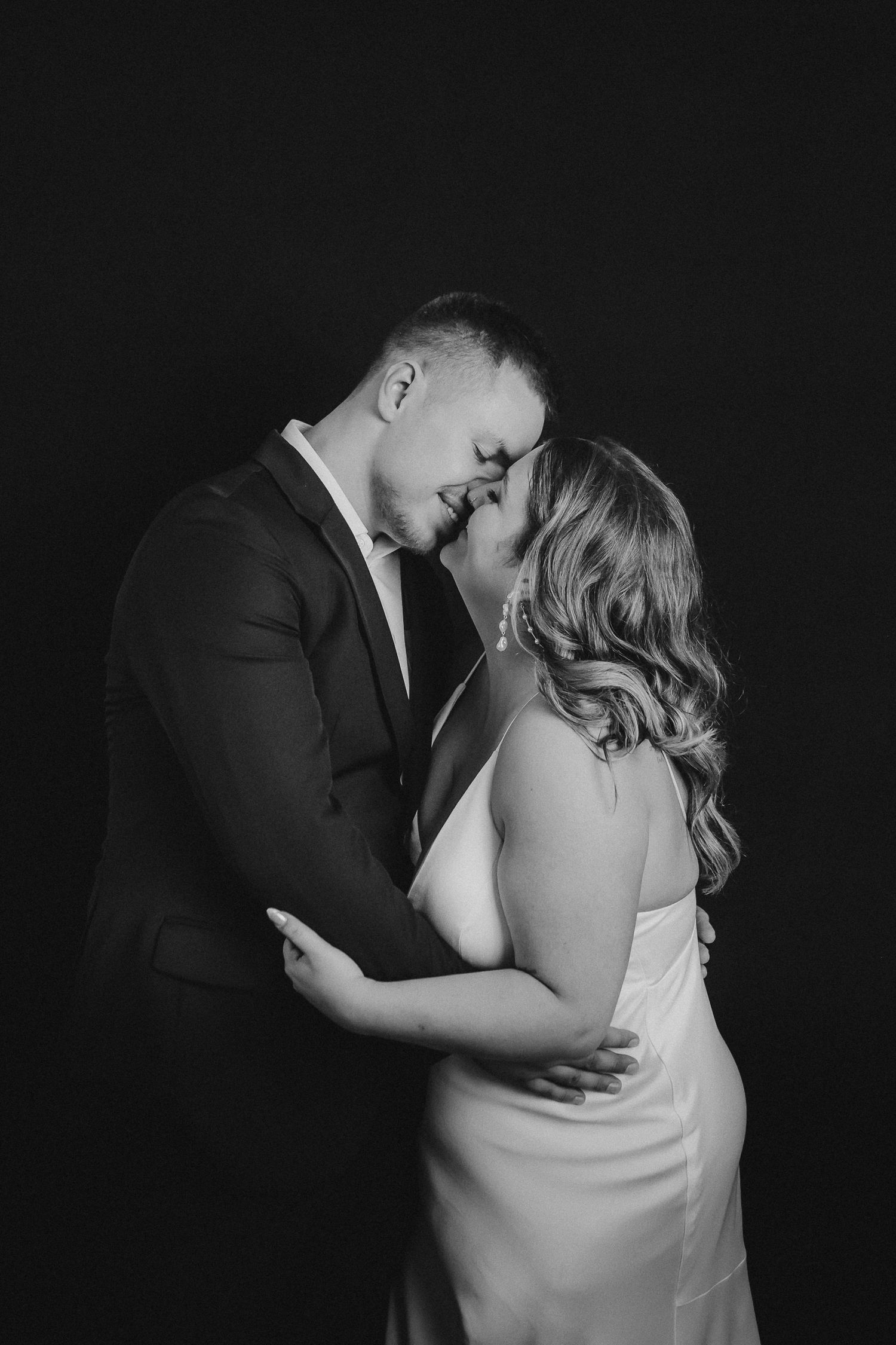 Intimate black and white portrait series showing tender romantic moments against dark background.