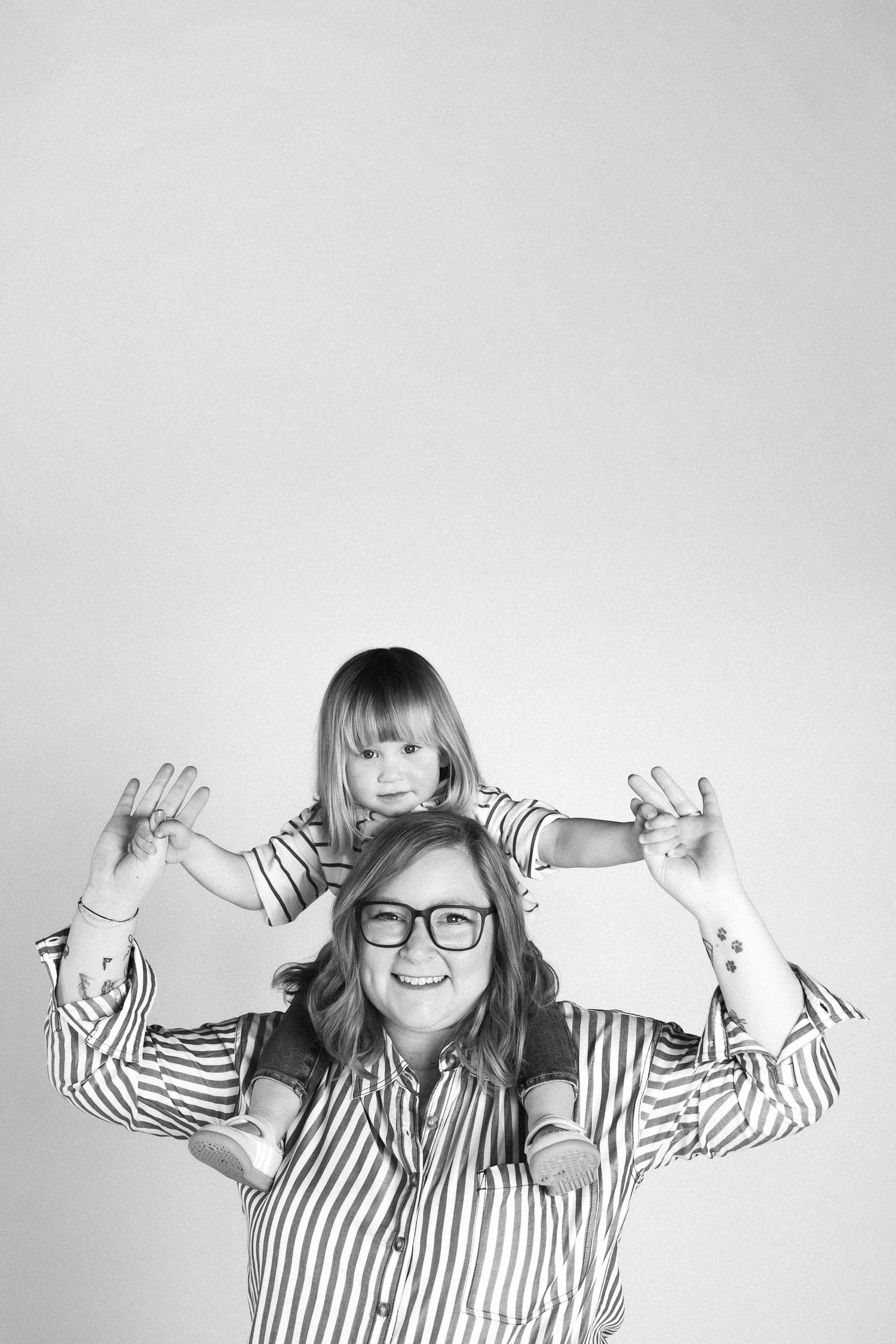 A black and white portrait shows a playful parent and child wearing matching striped shirts against a light background.