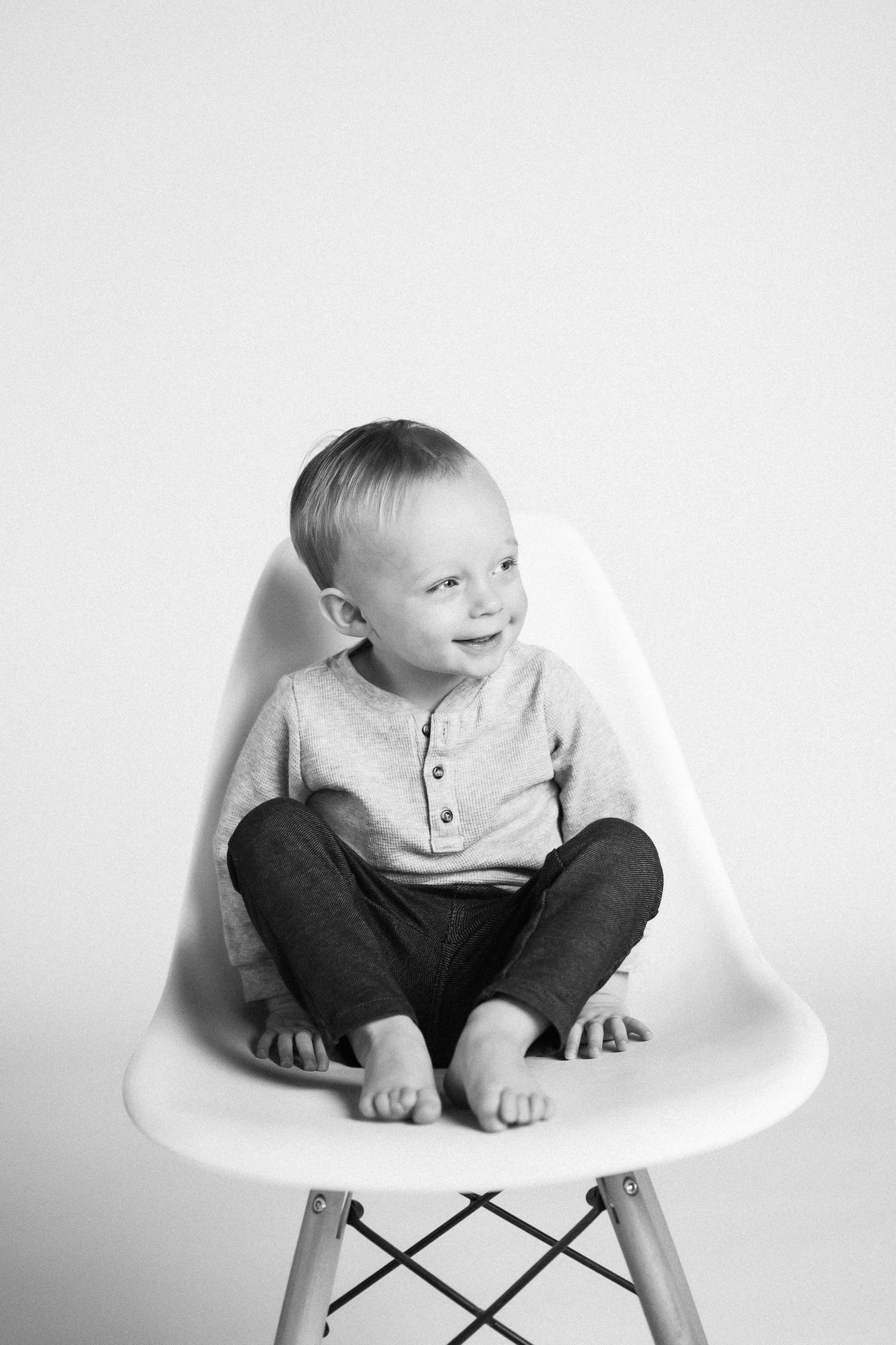 A sequence of black and white photos showing a small child sitting in a white Eames-style chair.