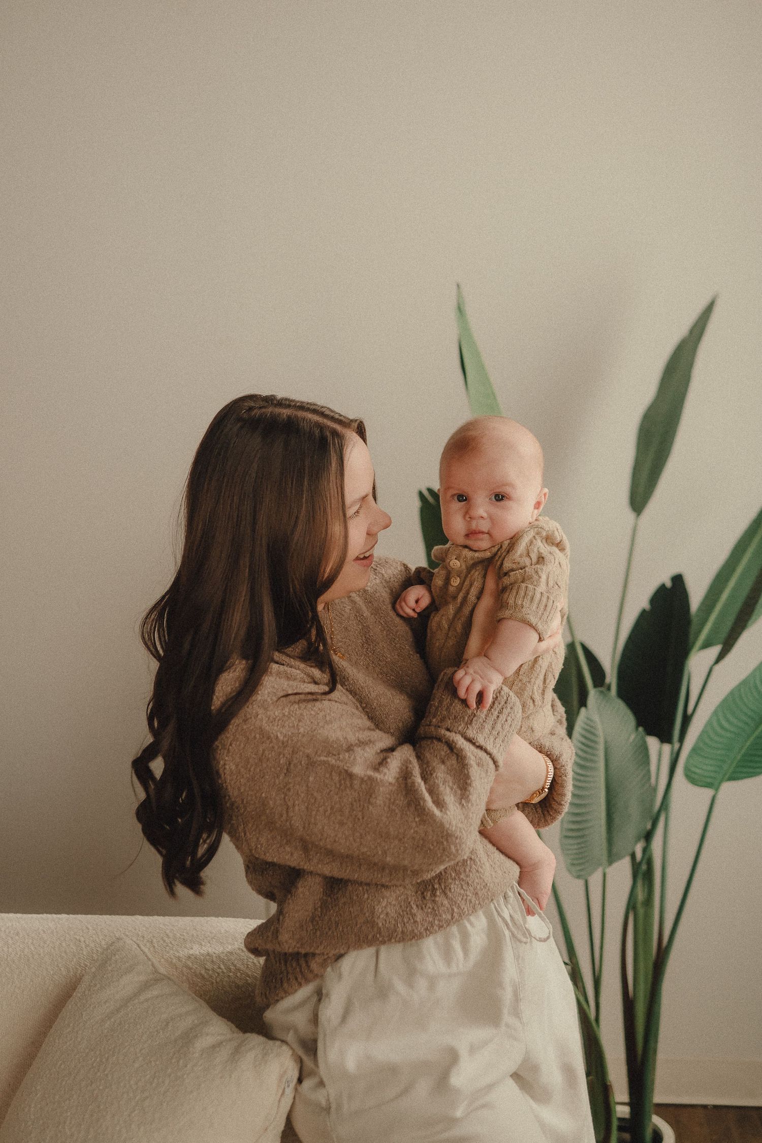 Intimate family portrait session showing tender moments with a baby against a neutral wall with green plants.