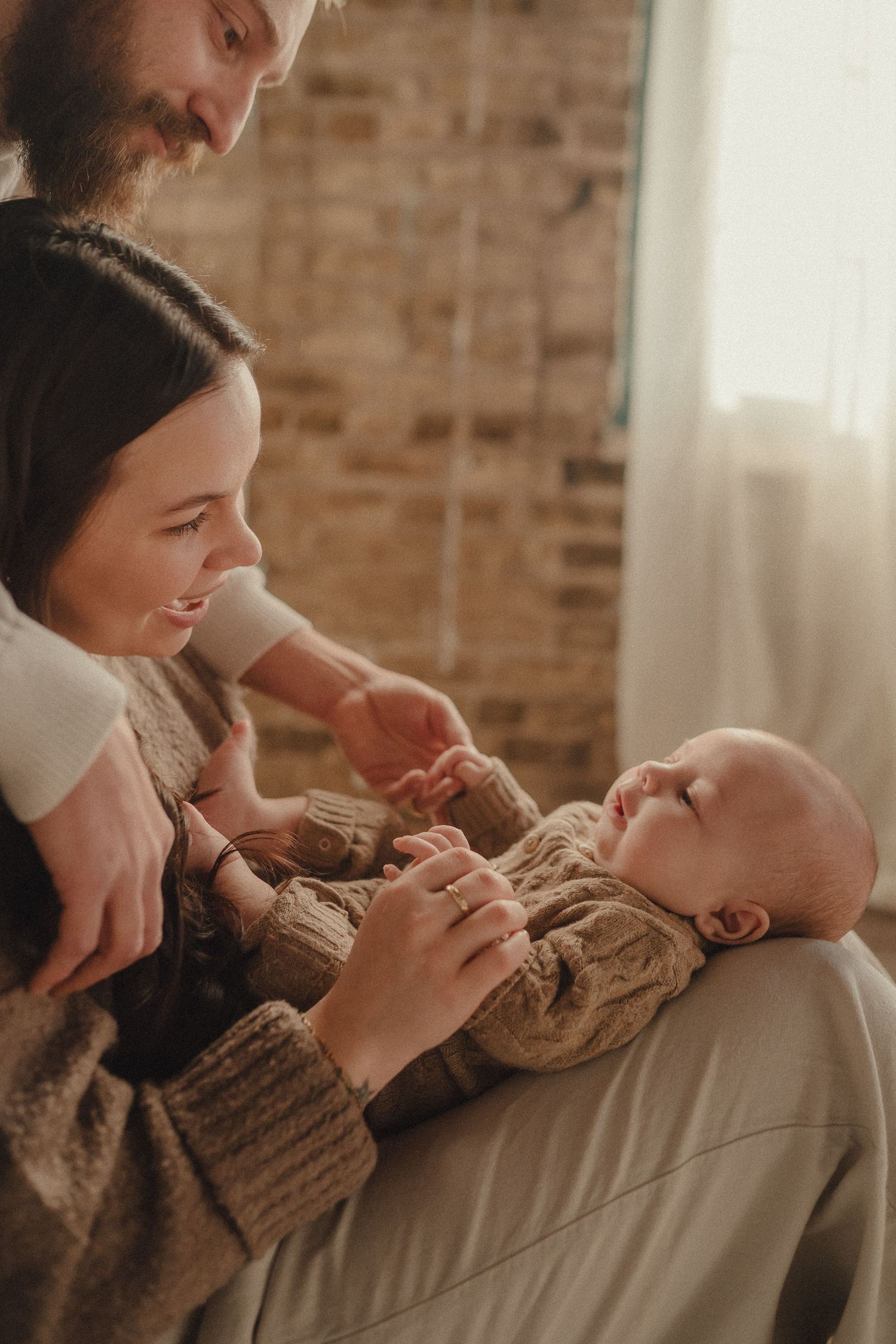 A tender family moment captured in warm tones showing affectionate interaction with a baby wearing a knit sweater.