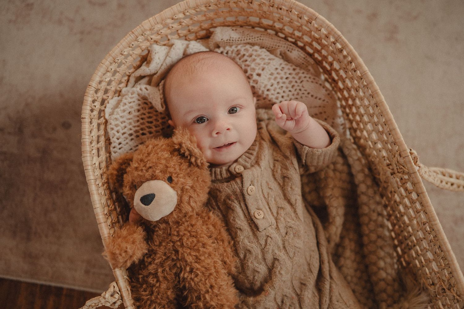 Baby lying in a woven basket surrounded by plush teddy bears and soft textiles.