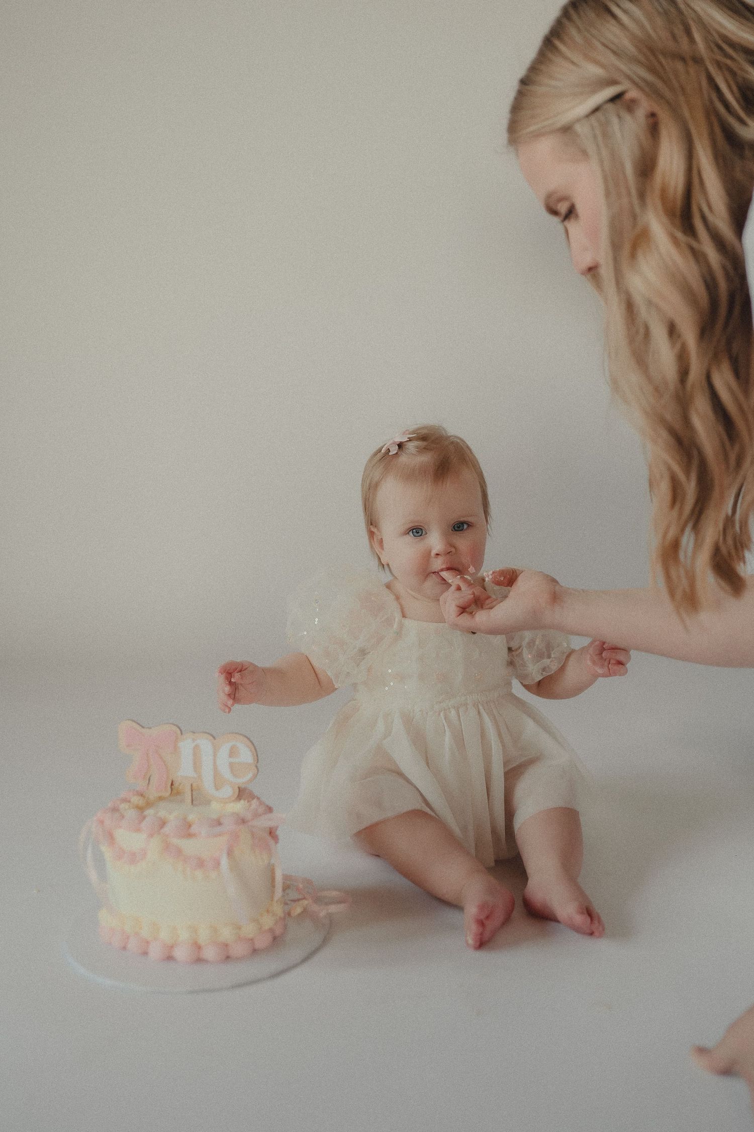 Mother feeding her baby girl cake during a first birthday cake smash photo session.