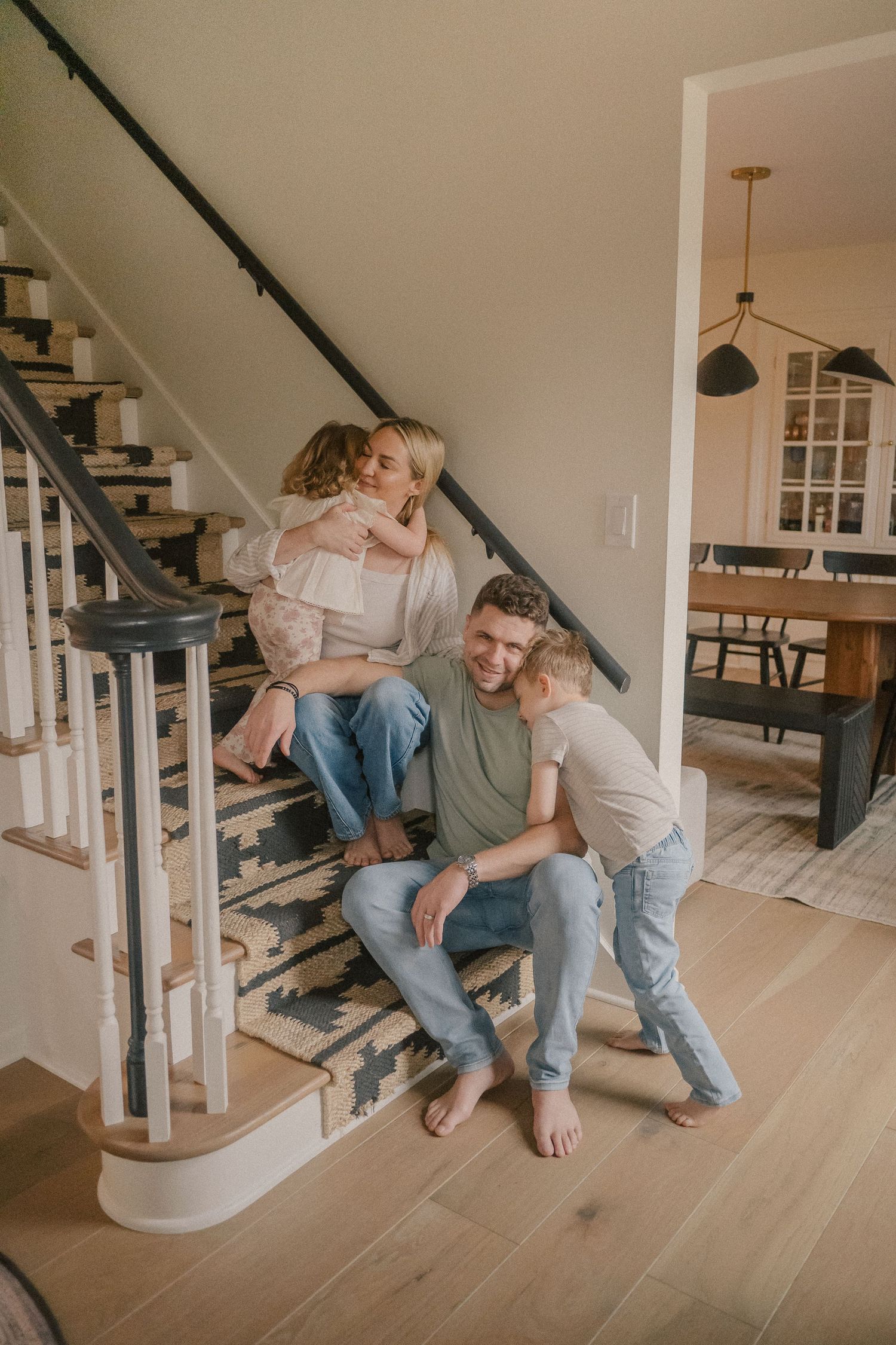 Happy family of four sitting together on staircase steps in a modern home interior.