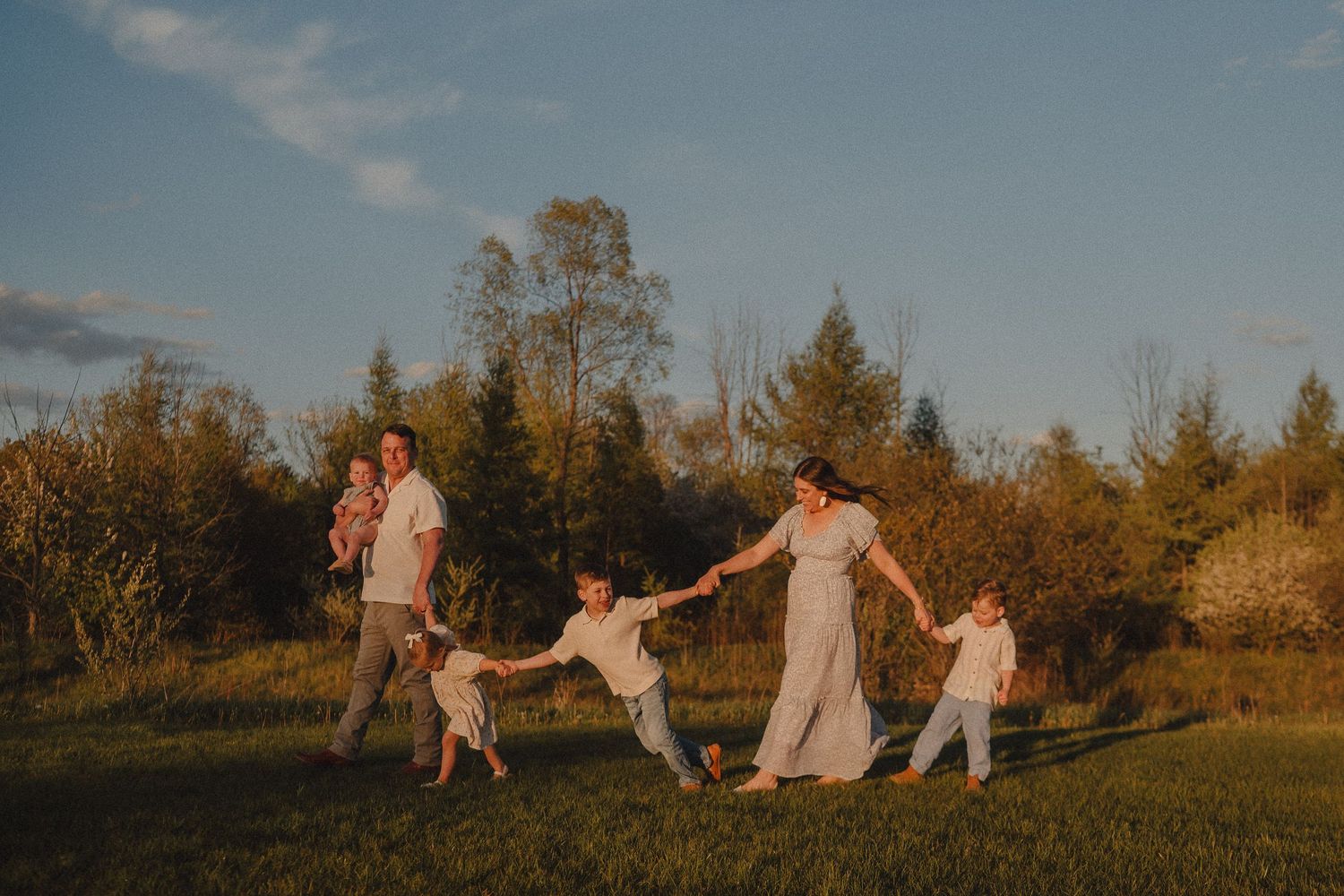 A joyful family holding hands and walking together in a sunny green meadow at golden hour.