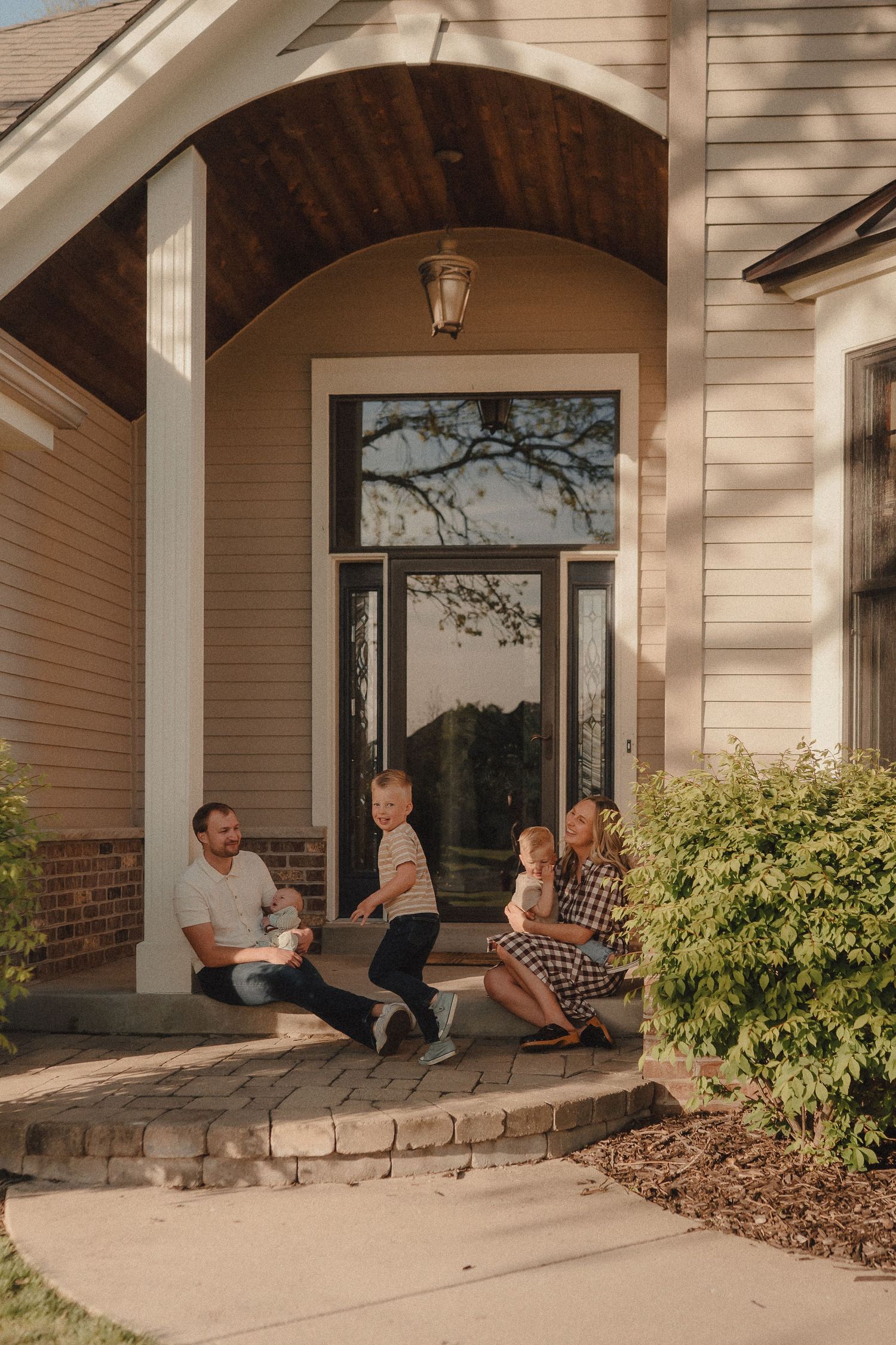 Family relaxing together on the front porch steps of their charming suburban home.