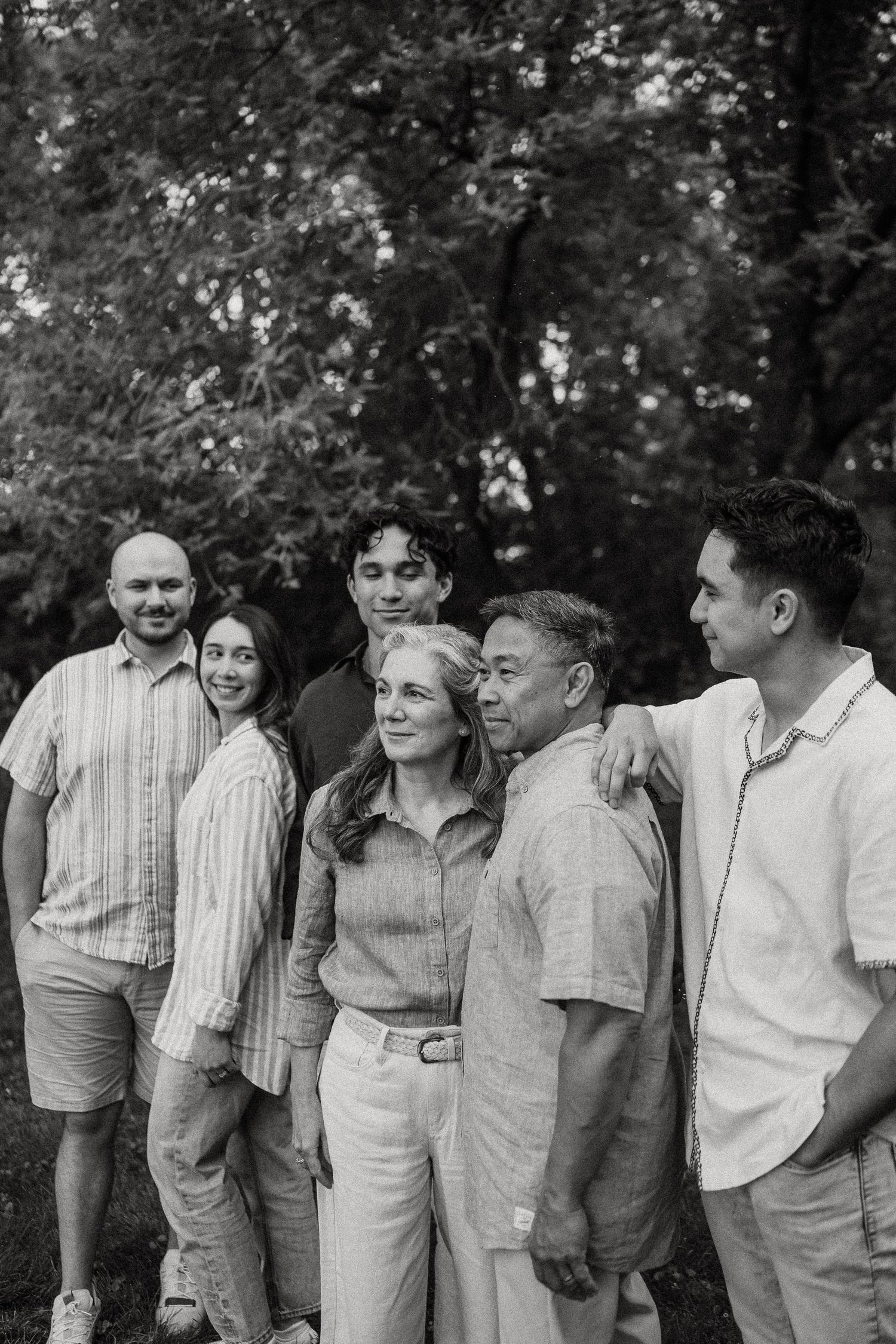 Black and white family portrait of six people smiling outdoors among lush trees.