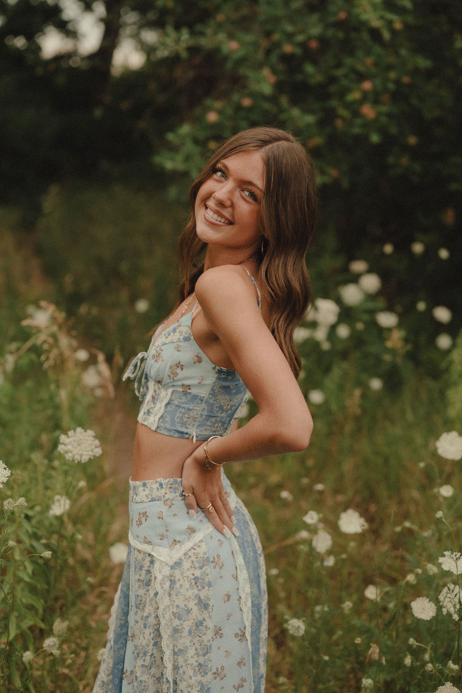 Smiling young woman in blue floral crop top and skirt posing in a wildflower meadow.