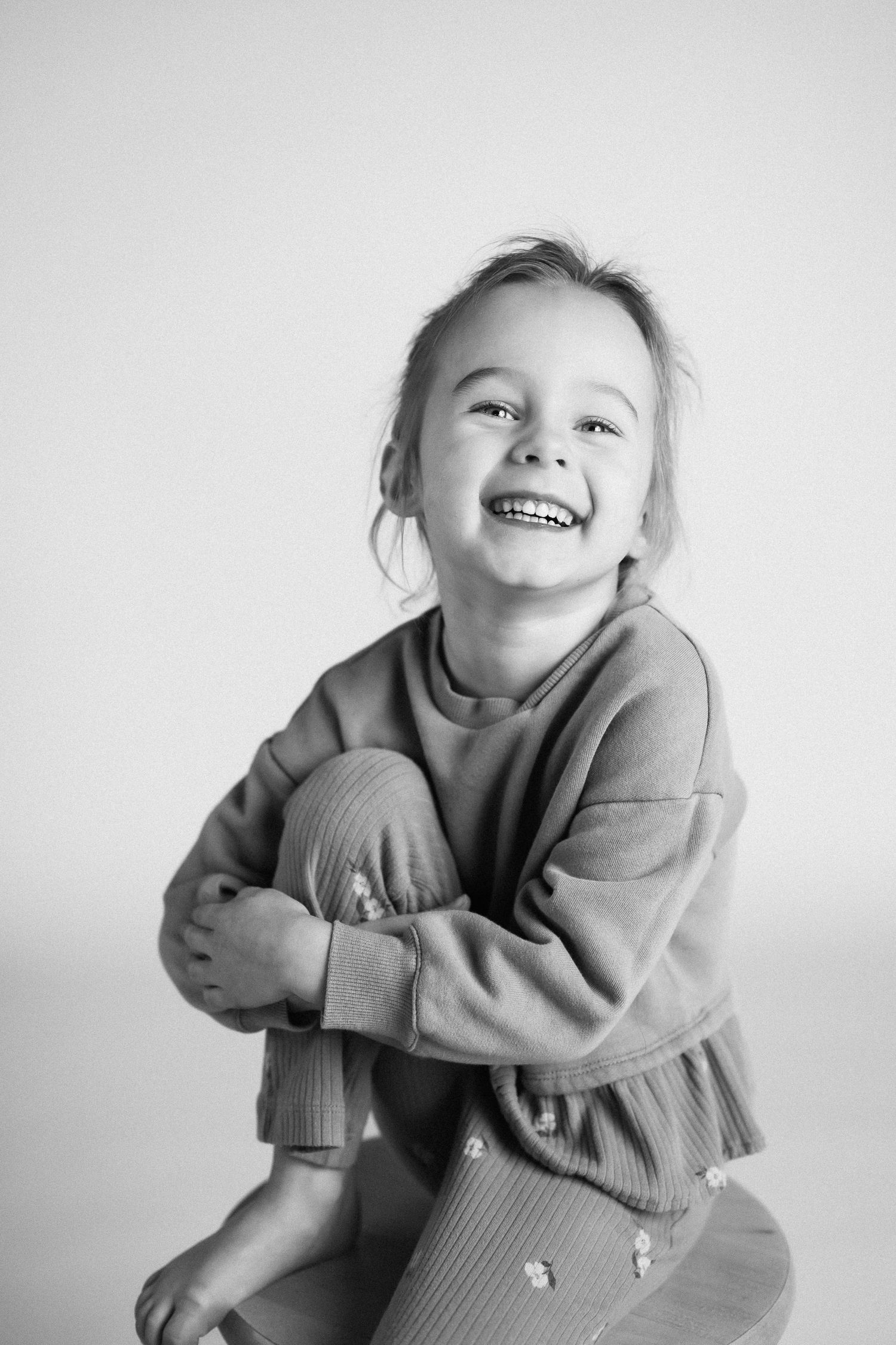 Black and white photo series showing joyful expressions and playful poses in a cozy sweater against white background.