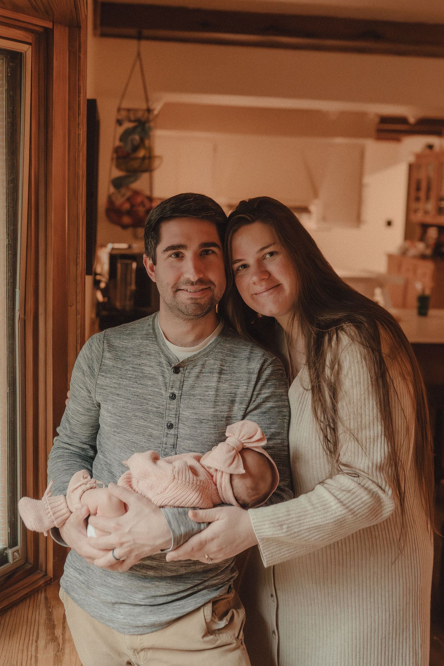 Intimate indoor family moment showing people in gray and white sweaters holding a baby.