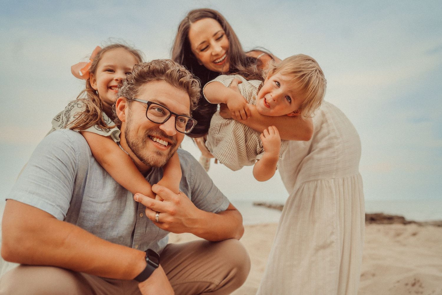 A happy family plays together outdoors in warm sunset lighting on a sandy beach.