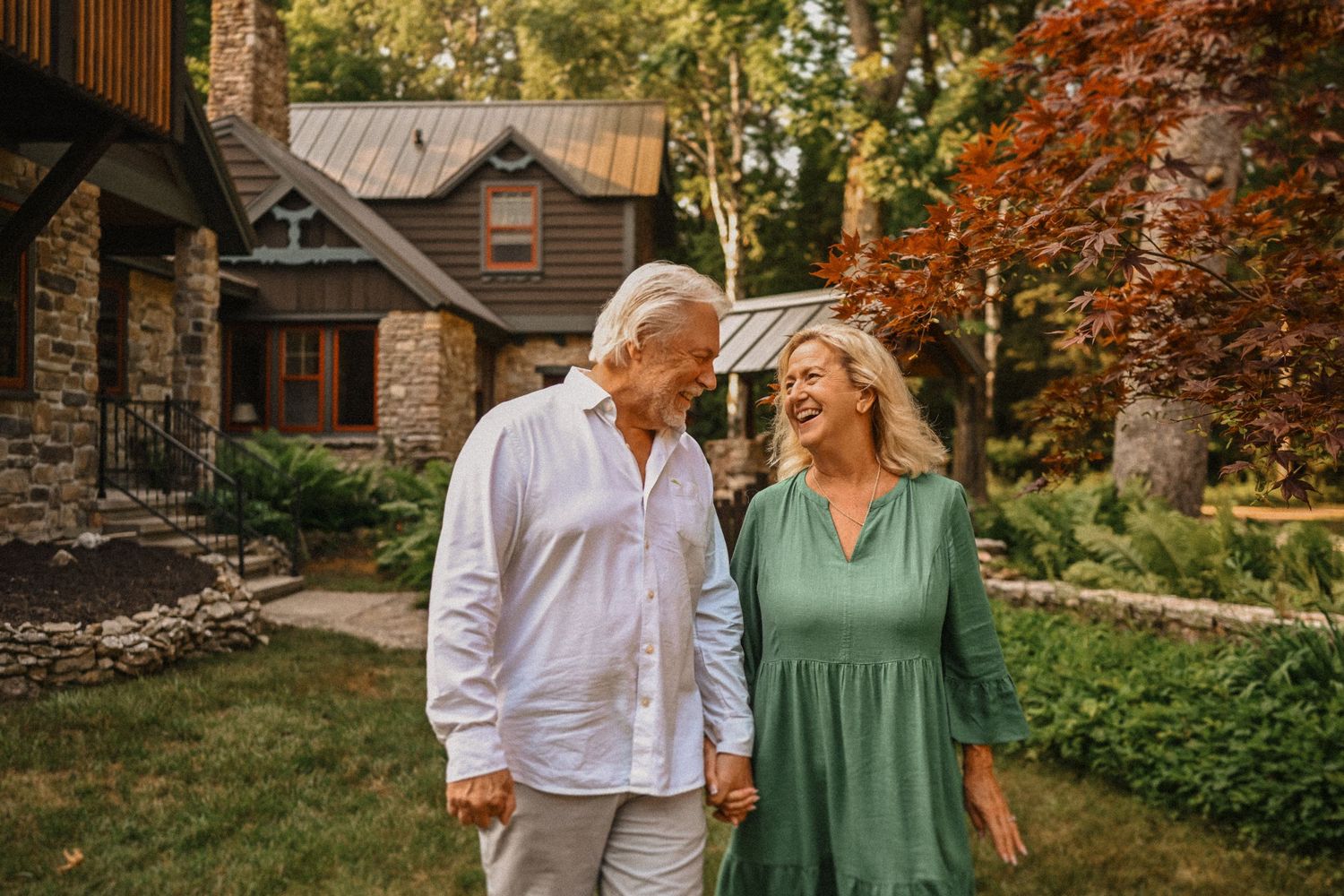 Couple in casual attire share tender moment outside their mountain cabin home.