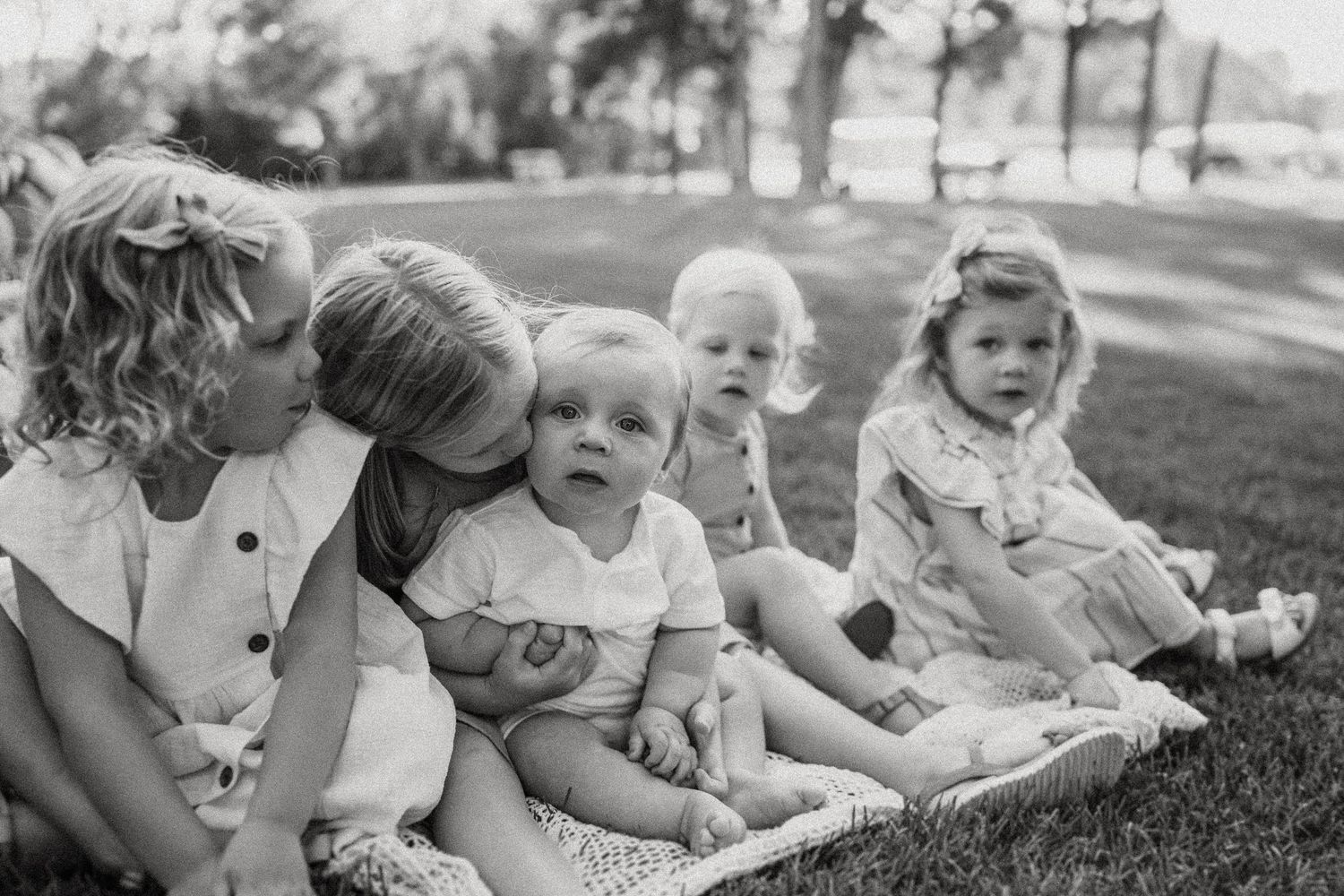 Black and white candid photo of children sitting together on grass outdoors.