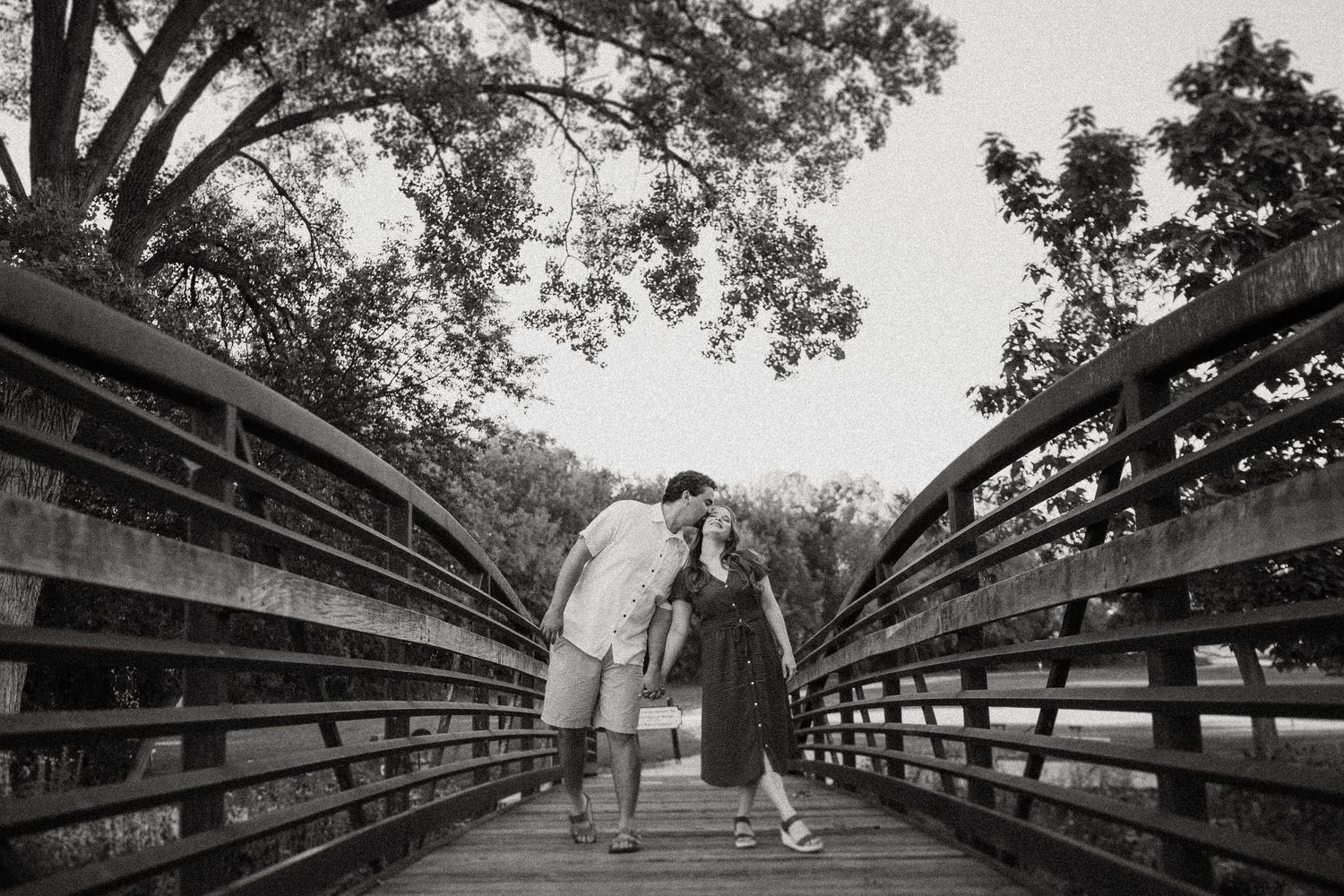 Black and white photo of couple walking together on wooden bridge pathway.