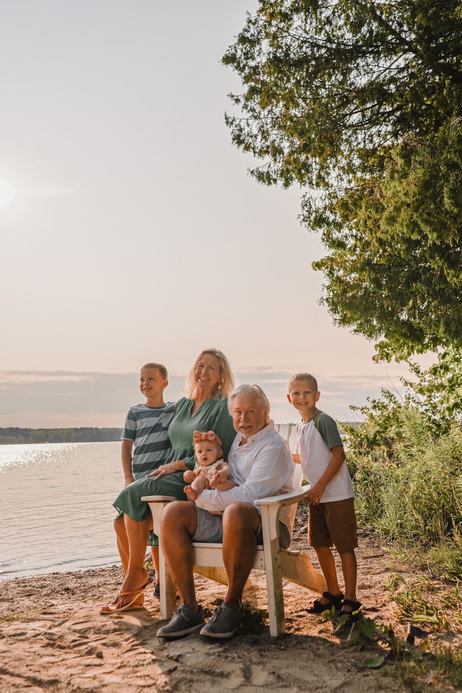 Multi-generational family group gathered on a beach during sunset with lake views.