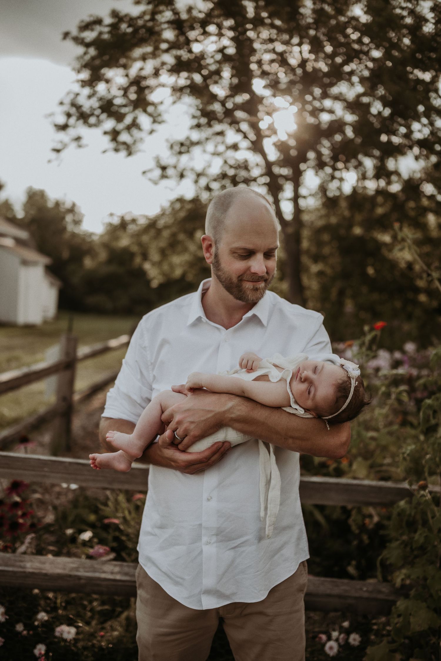 A tender moment captured in golden light as a parent cradles a newborn baby in a garden setting.