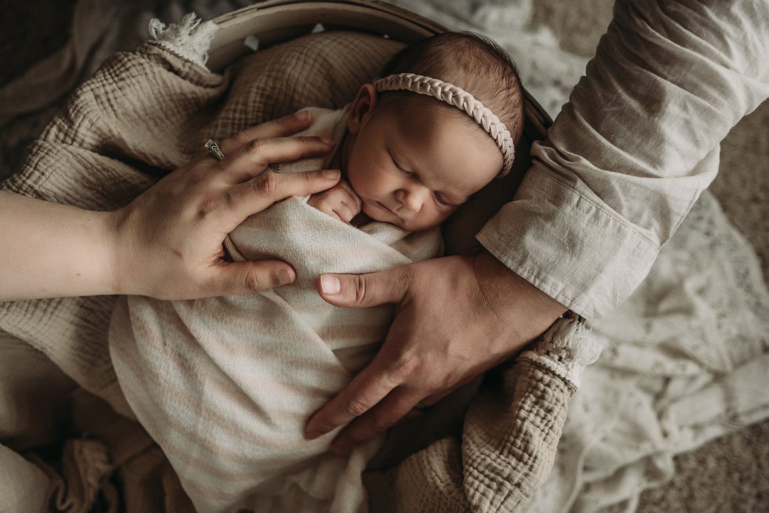 Gentle hands caress a peaceful sleeping newborn swaddled in soft fabric.