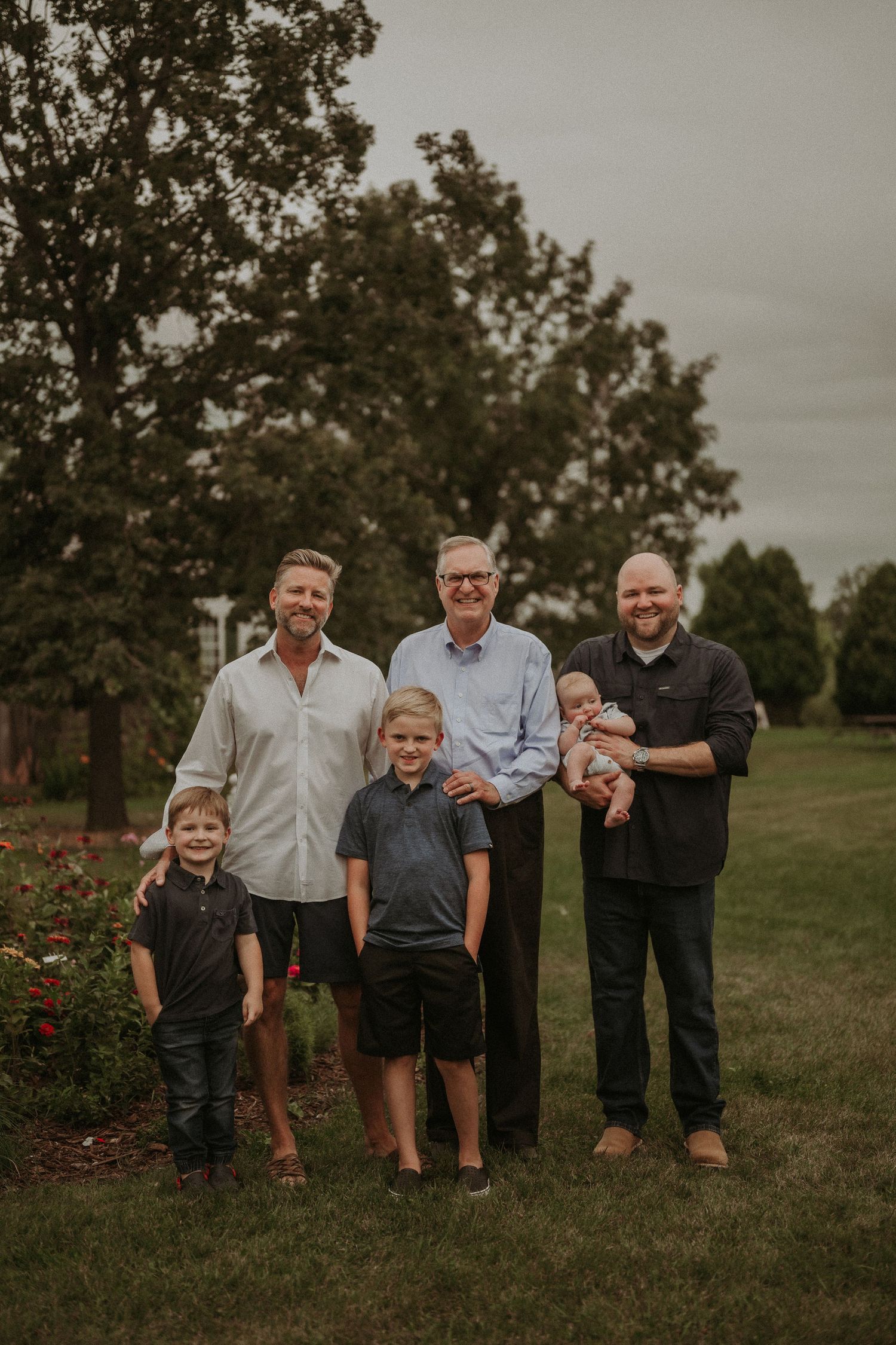 Family group of men and children gather for a portrait in a garden with blooming roses.