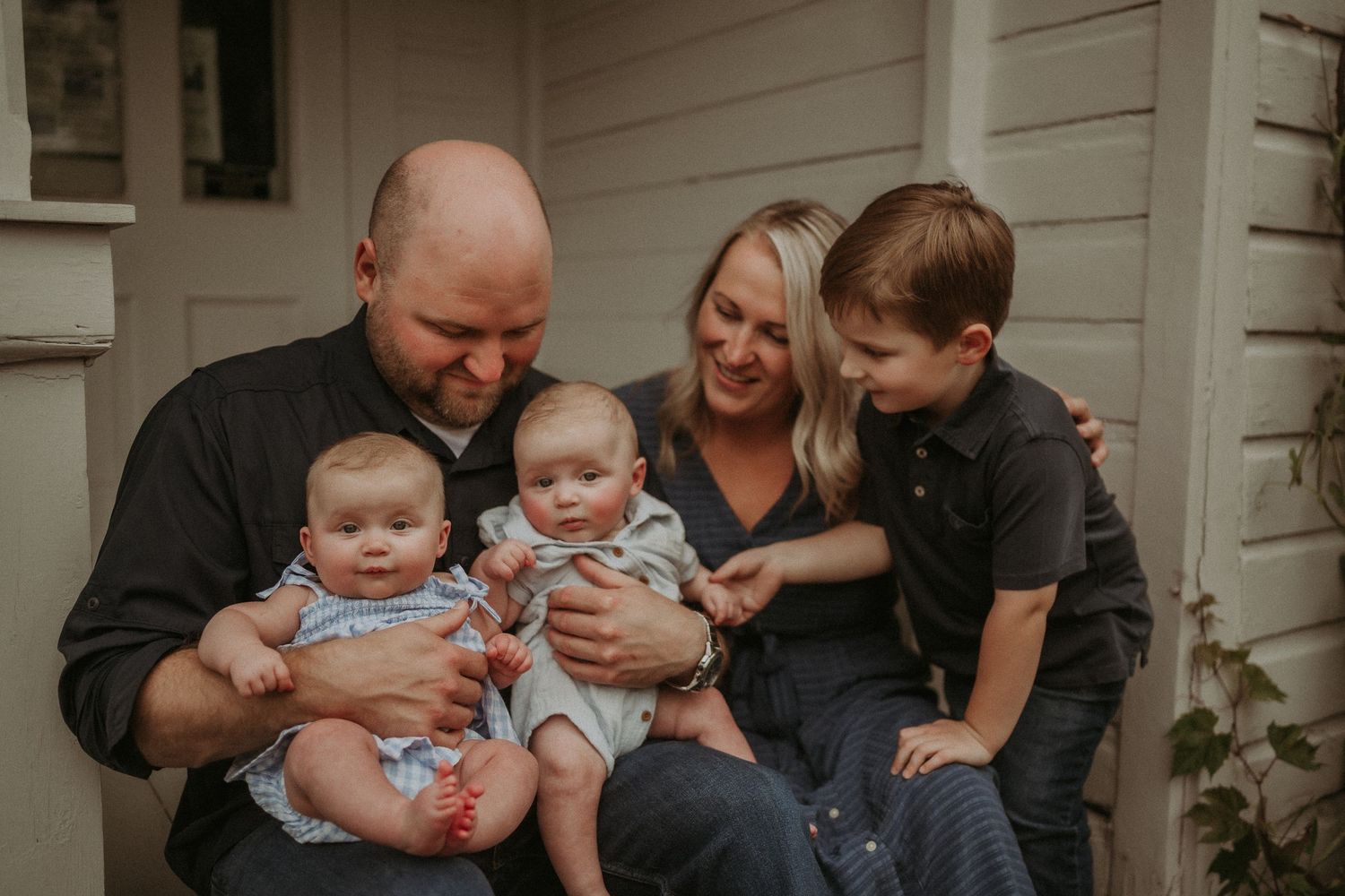 Intimate family portrait on porch steps with parents holding twin infants and older sibling.